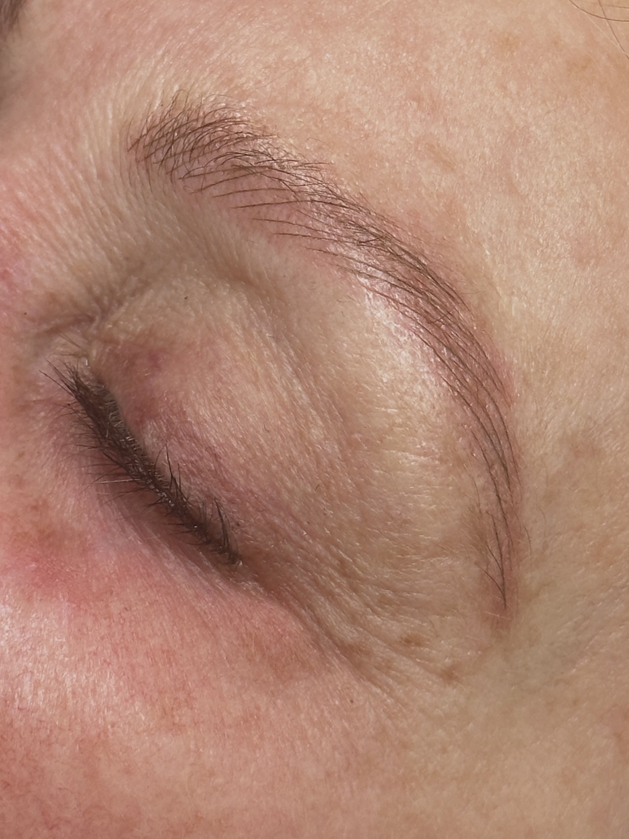 Close-up of a closed eye with visible eyelashes and eyebrow, skin texture, and fine lines.