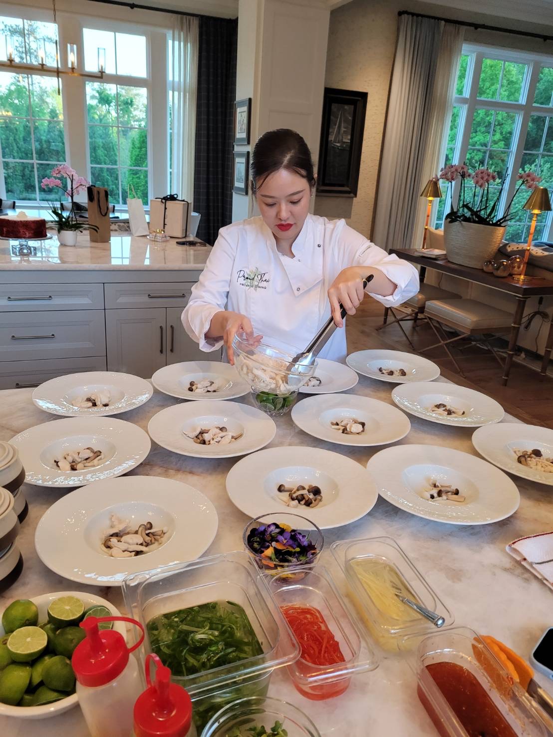 Young woman preparing dishes in a bright kitchen with multiple plates and ingredients on the counter.