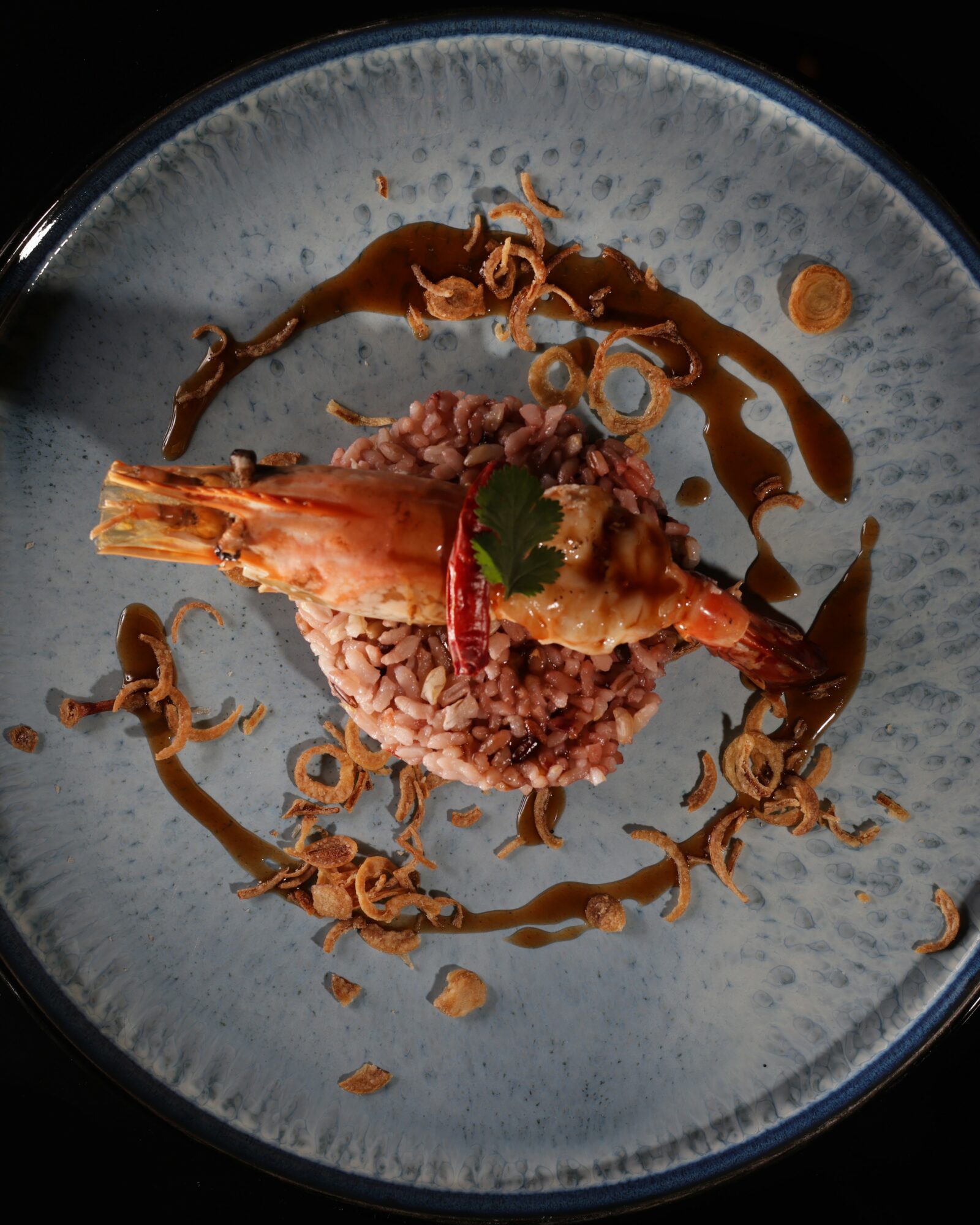 Plate with cooked shrimp, rice, sauce, and garnishes, arranged artistically on a blue dish.