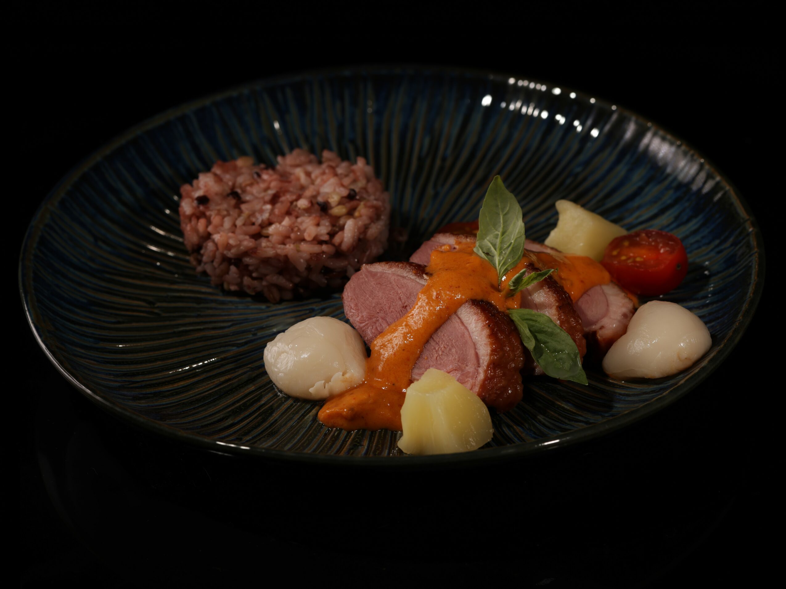 Plate with cooked meat, vegetables, and rice, garnished with herbs and cherry tomato, on a dark background.
