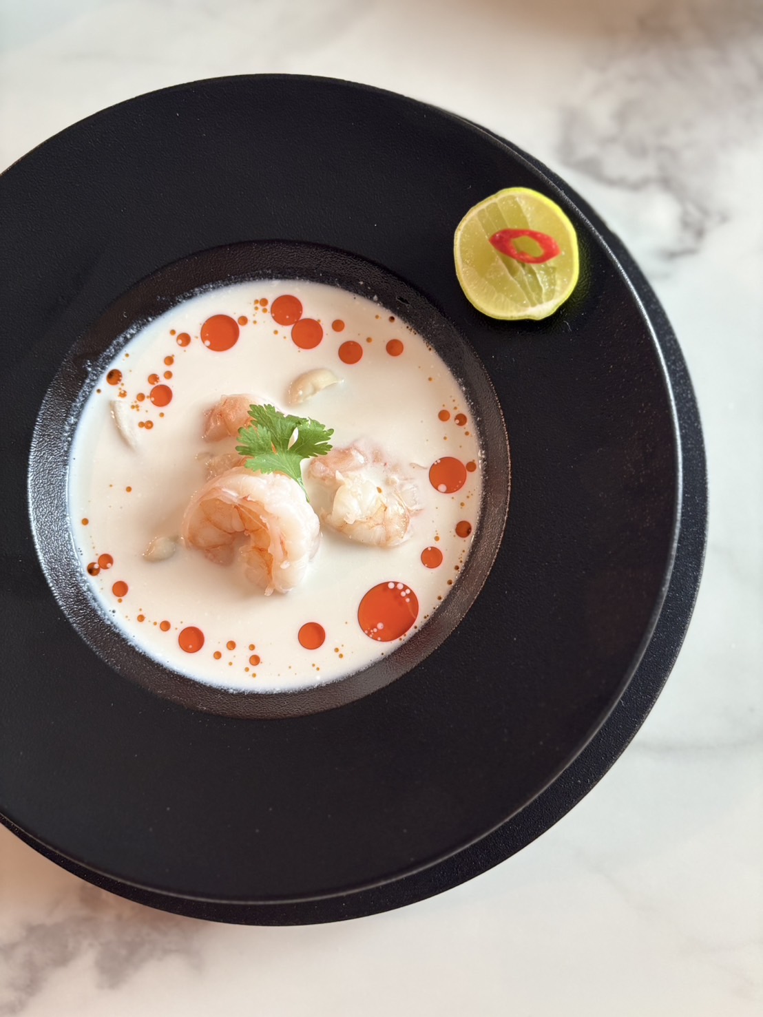 Bowl of creamy soup with shrimp, garnished with cilantro, on a black plate with a lemon slice on the side.