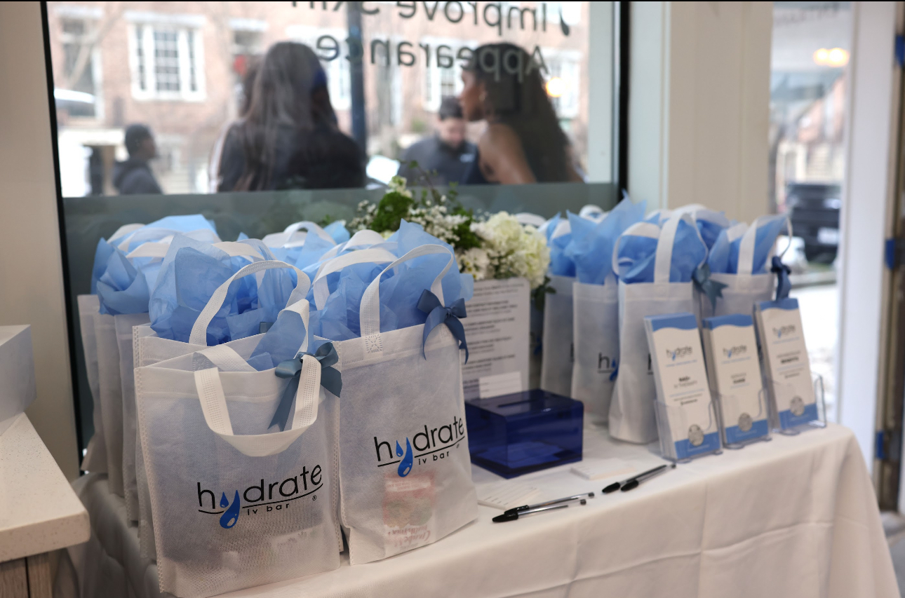 Table with hydration gift bags, a box, and informational cards inside a store window, with people outside visible through the window.