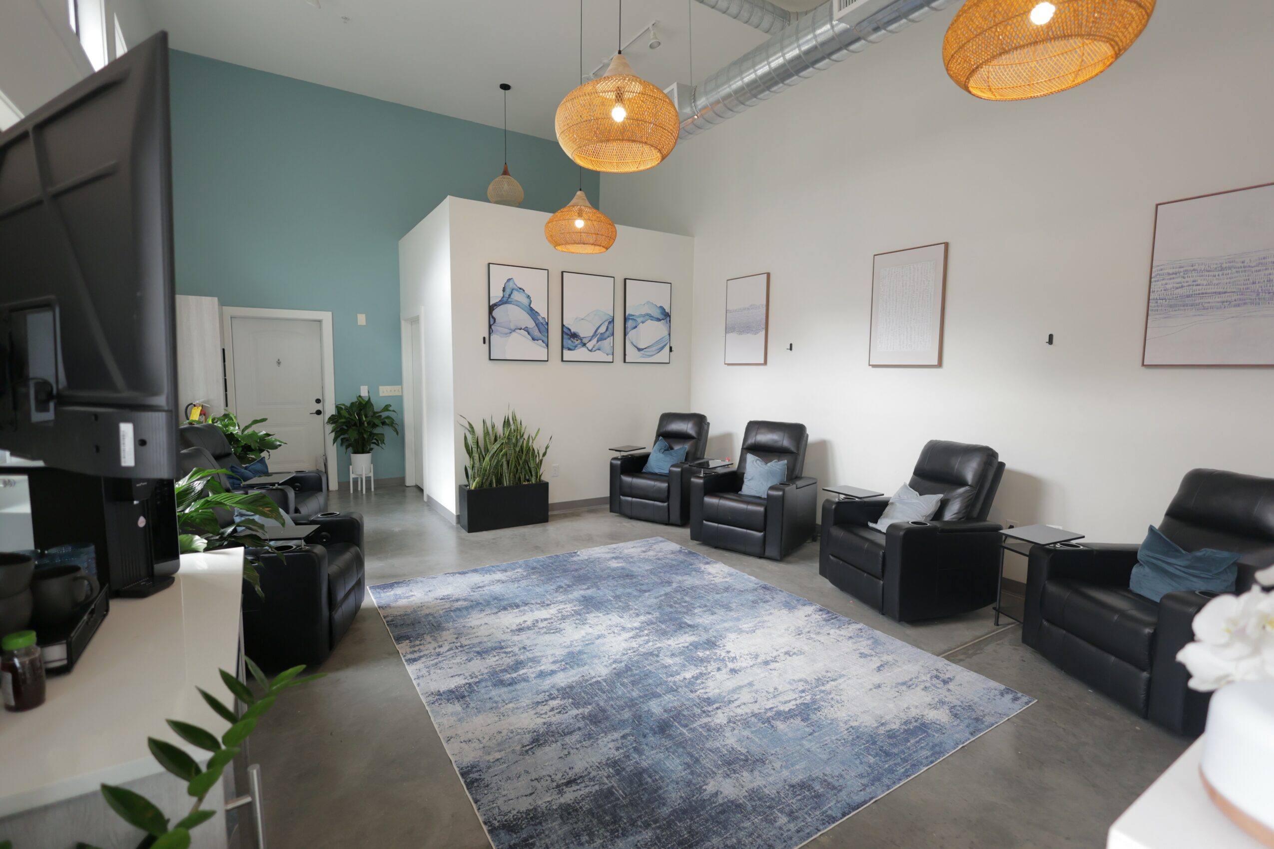 Waiting room with four black chairs, a blue and gray rug, and framed artwork on white walls.