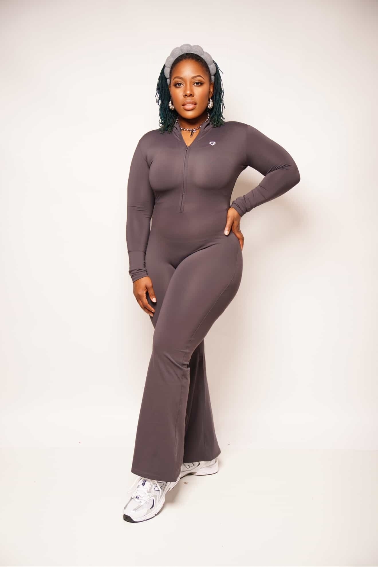 Woman in a fitted, long-sleeve jumpsuit standing against a plain background, with one hand on her hip.