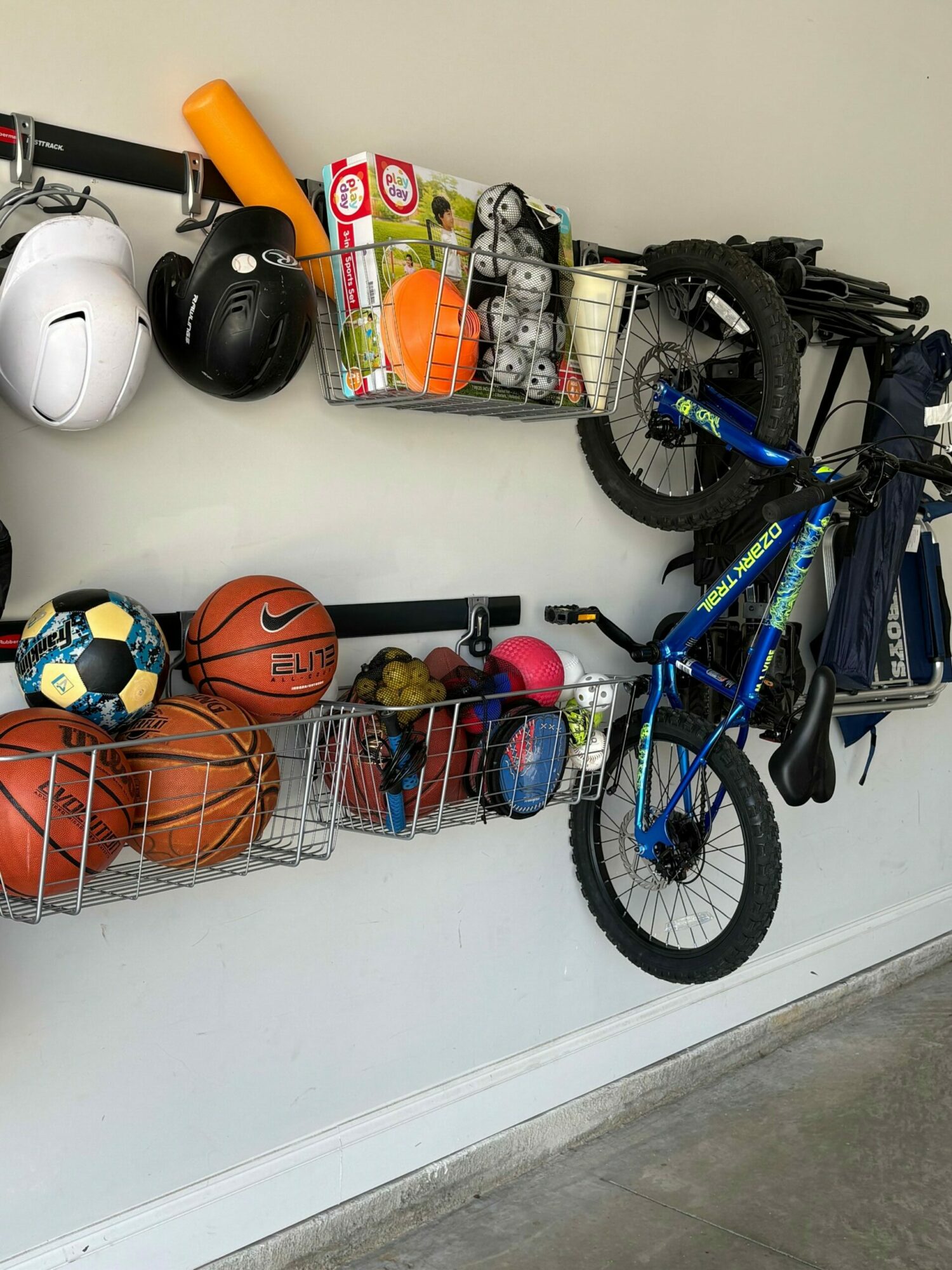 Bicycle, basketballs, soccer ball, helmets, and various toys on a black shelf against a white wall.