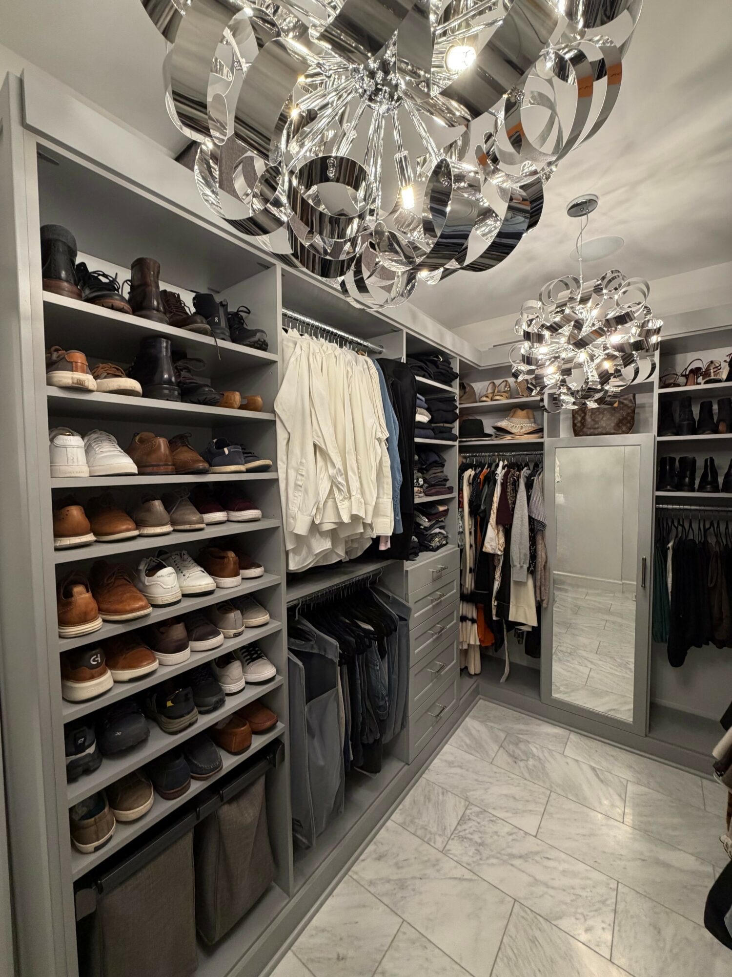 Walk-in closet with shelves of shoes, clothing, and a mirror, illuminated by decorative ceiling lights.