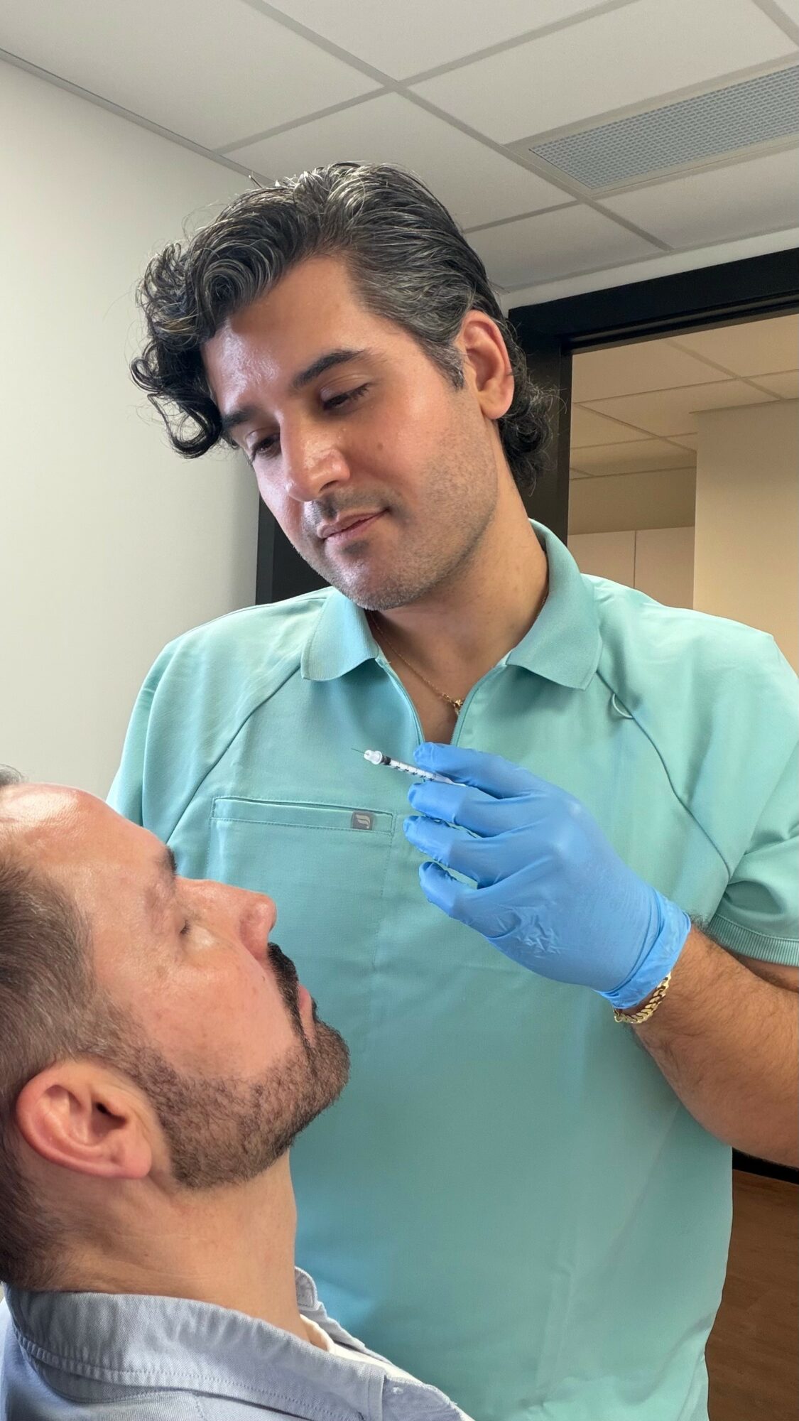 Medical professional in scrubs and gloves examines a patient's face in a clinical setting.