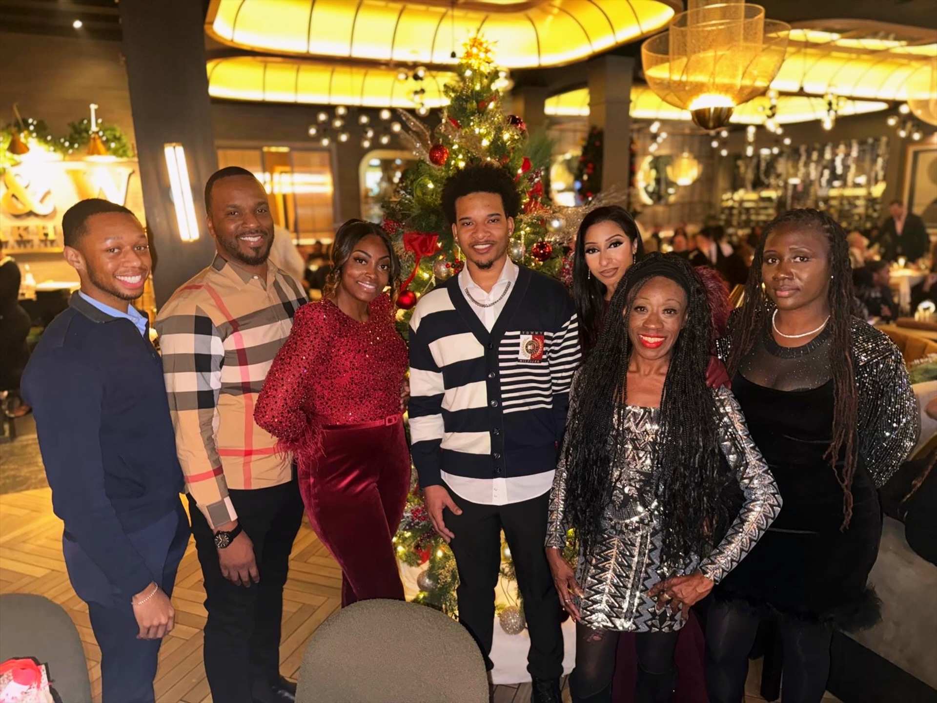 Group of seven people standing in front of a decorated Christmas tree in a festive setting.