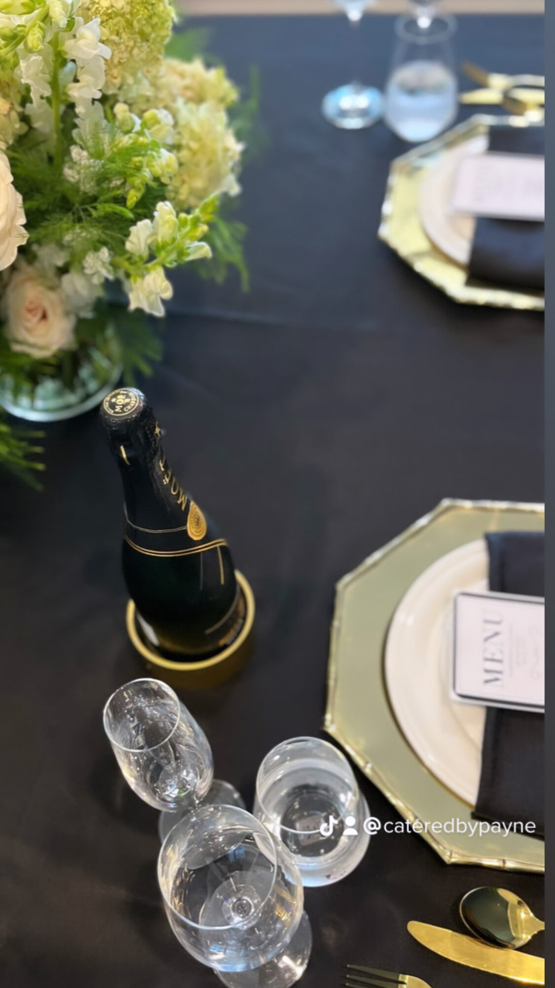 Table setting with a flower arrangement, champagne bottle, glasses, and gold-rimmed plates and cutlery.