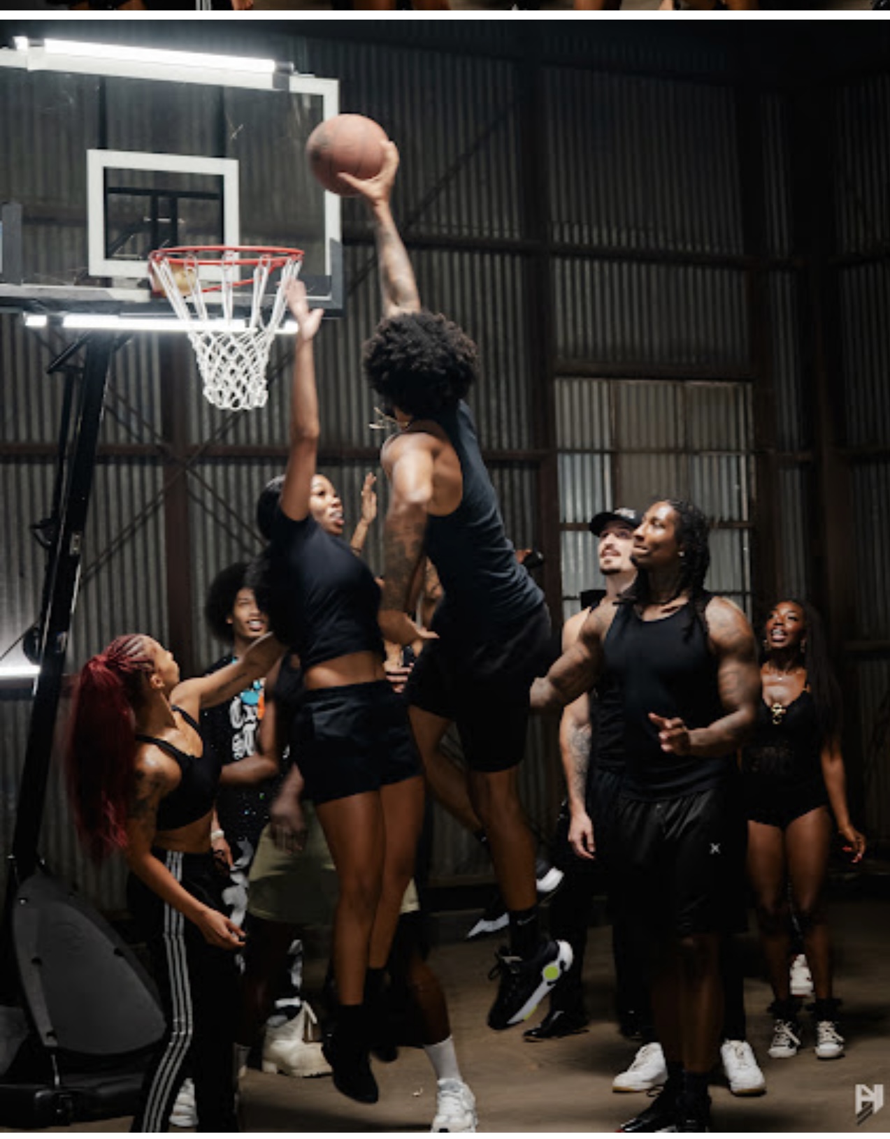 Group of women playing basketball indoors, one jumping to shoot the ball, others watching and cheering.