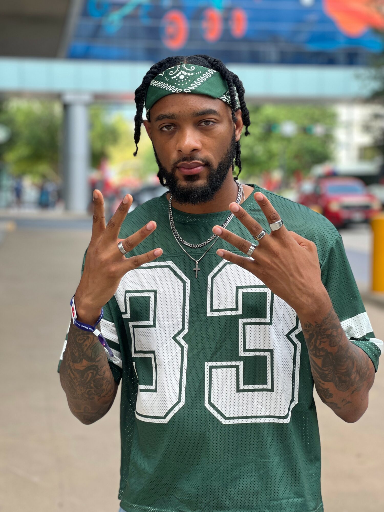 Young man with a green bandana, beard, and tattoos, wearing a green sports jersey with the number 93, outdoors.