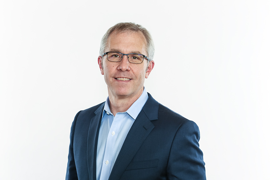 Man with glasses in a suit smiling against a white background.