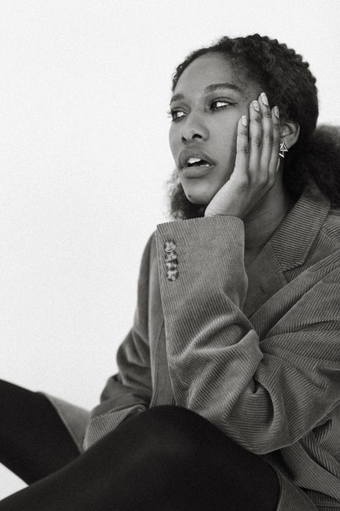 Woman with hand on face, wearing blazer, looking to the side, in black and white.