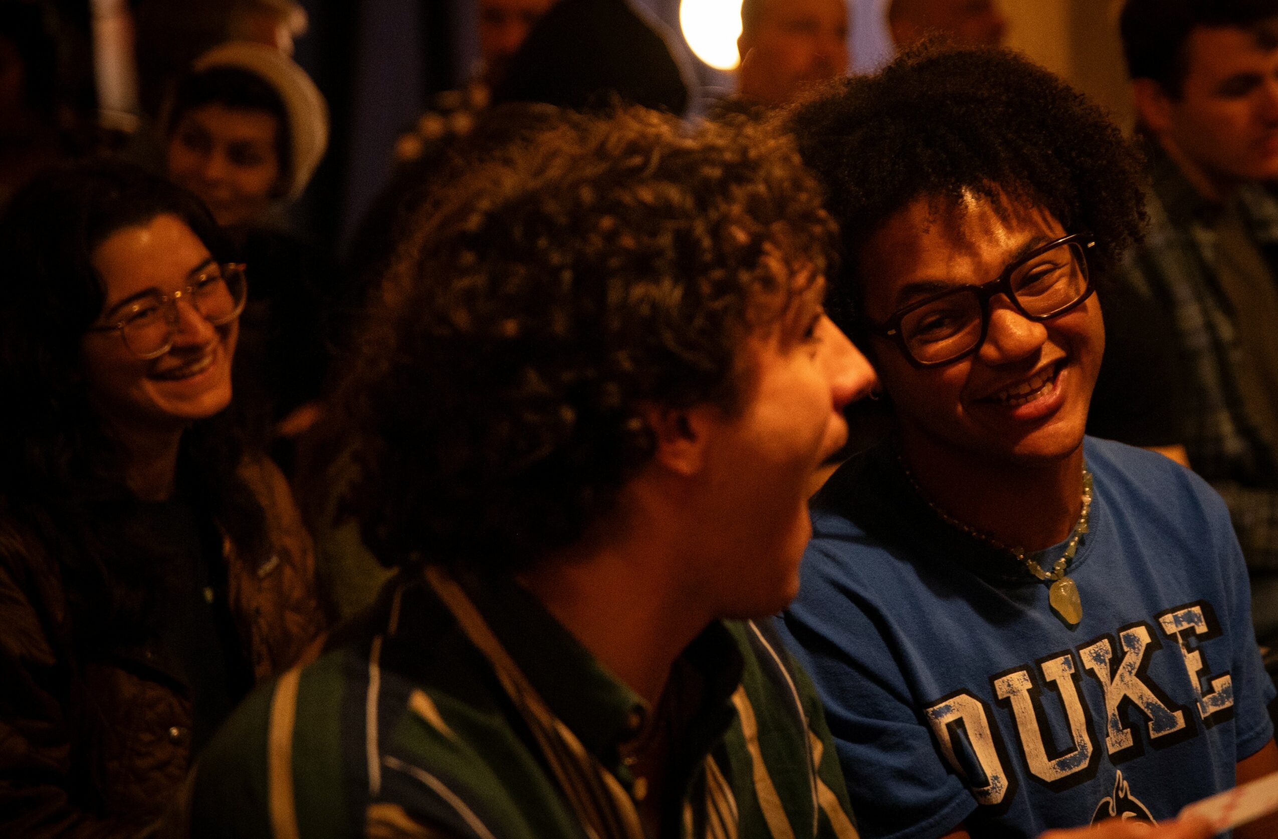 Group of people smiling and talking at an indoor event, with warm lighting and a lively atmosphere.