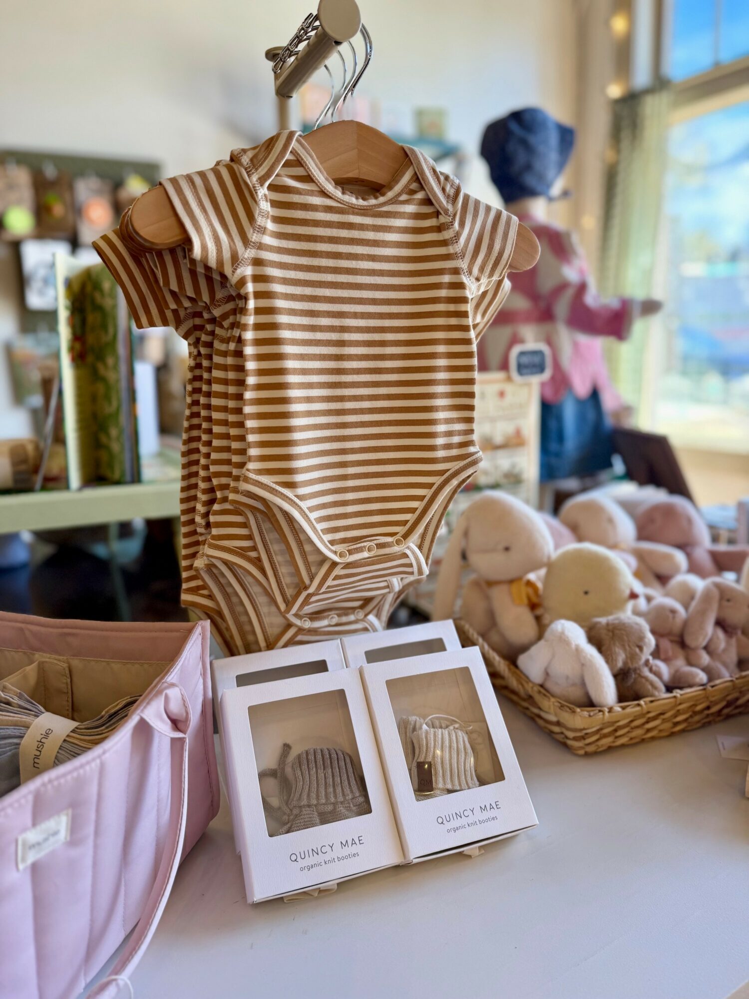 Striped baby onesie hanging on a wooden hanger, displayed on a table with plush toys and photo cards nearby.