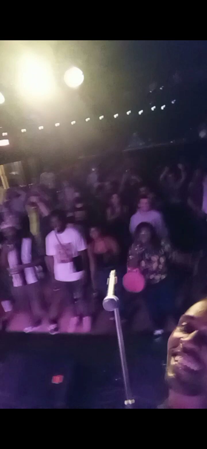 Crowd of people at an indoor event with bright lights overhead, some facing the camera, others turned away.