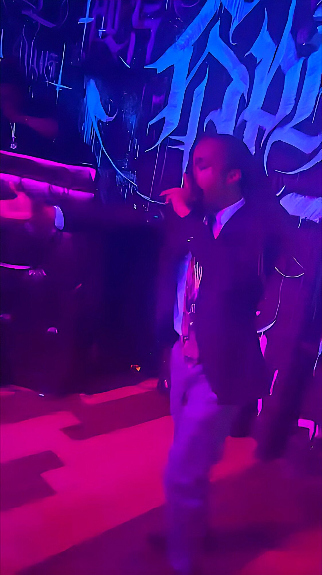 Person dancing in a dark room with colorful neon lights and graffiti-style wall art.