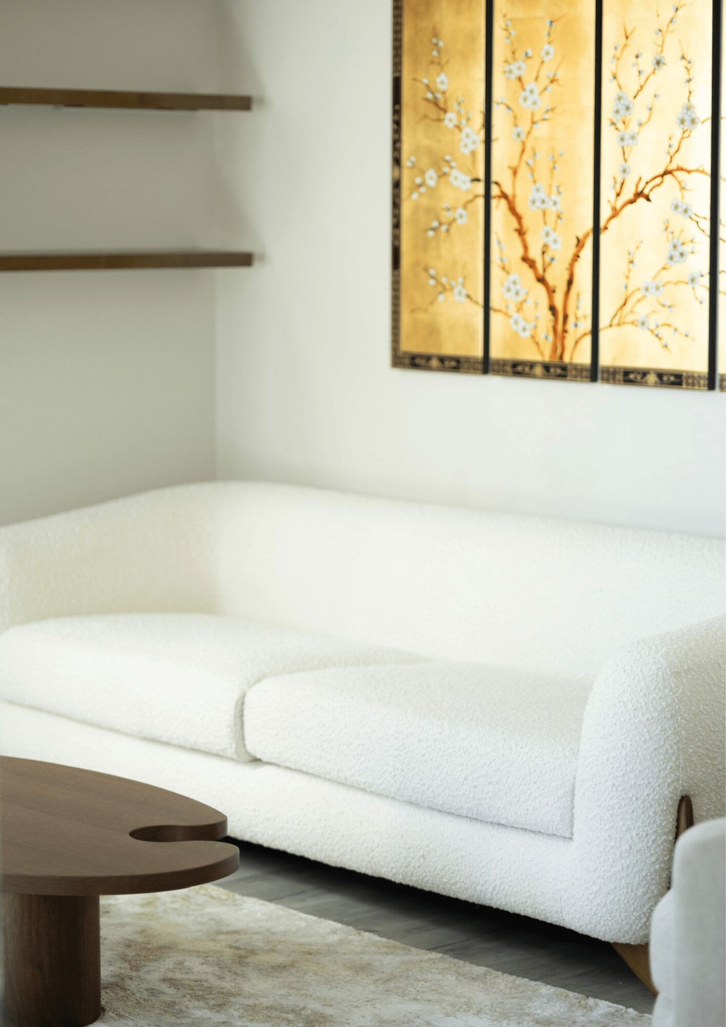 White sofa in a room with wall art and floating shelves, wooden coffee table in front.