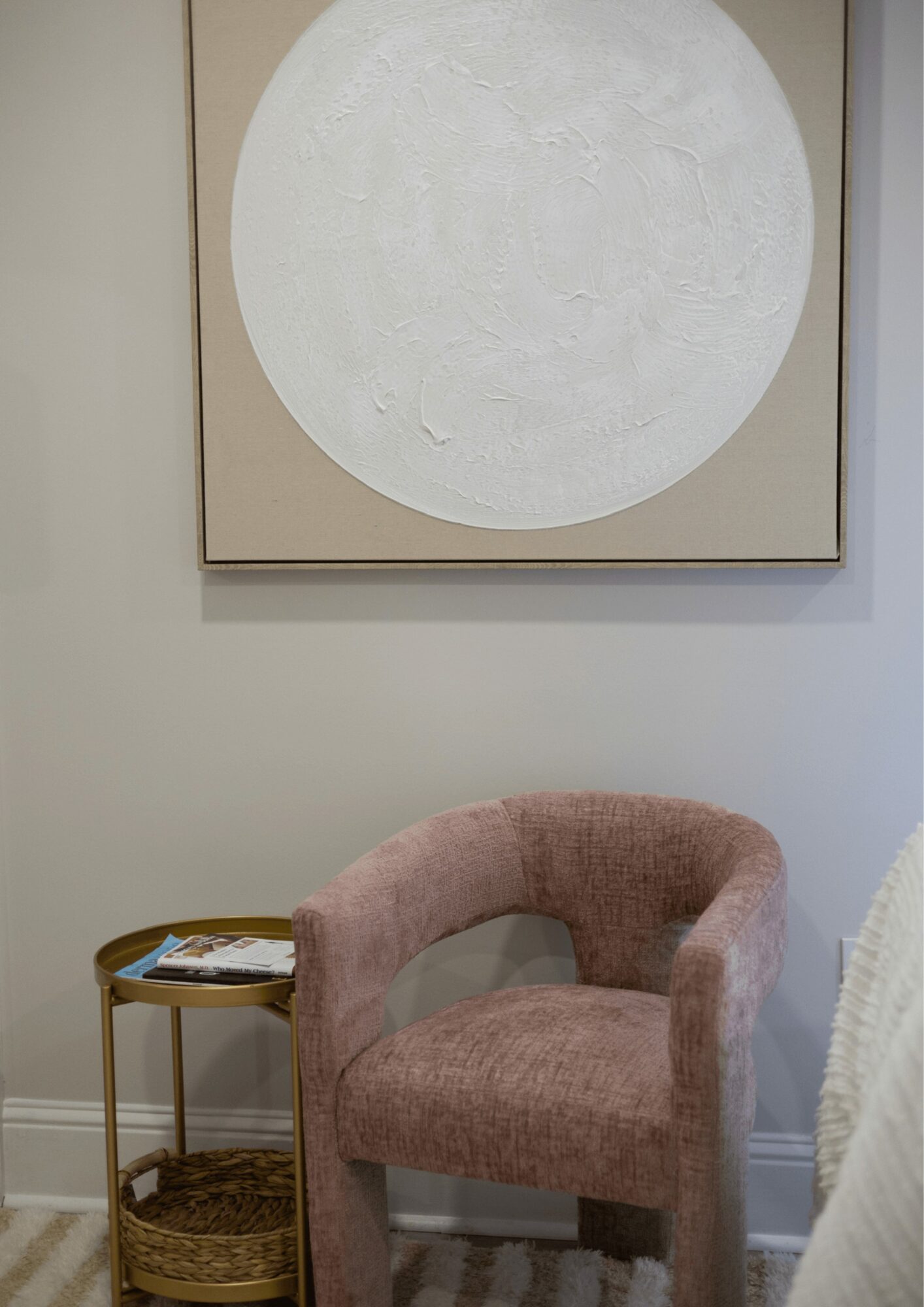 Pink upholstered armchair with a curved back and armrests, next to a small gold side table with magazines.