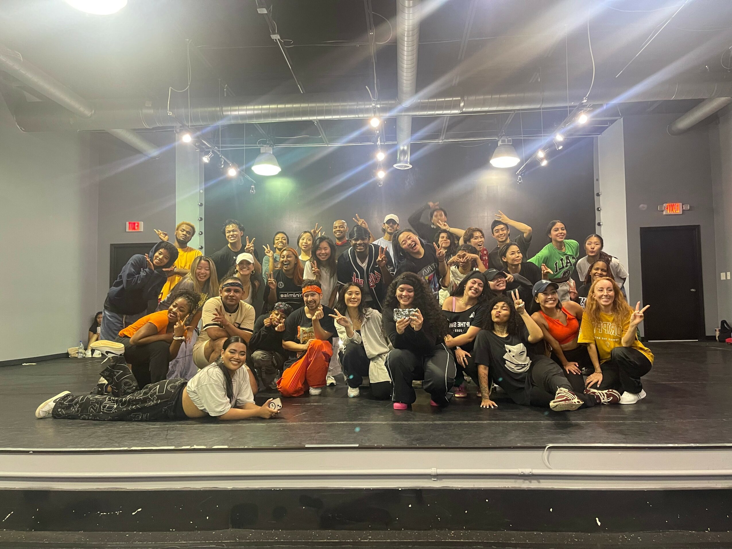 Group of people posing on stage in a dance studio with lighting and a dark background.