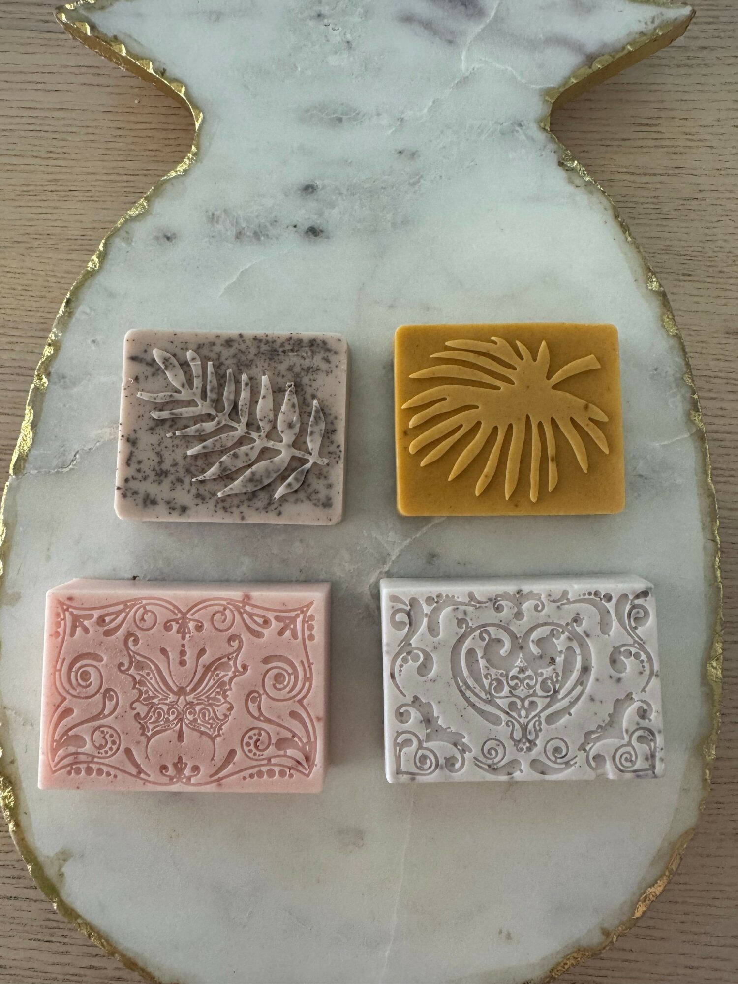 Four decorative soaps with leaf, tropical, floral, and heart patterns on a marble tray.