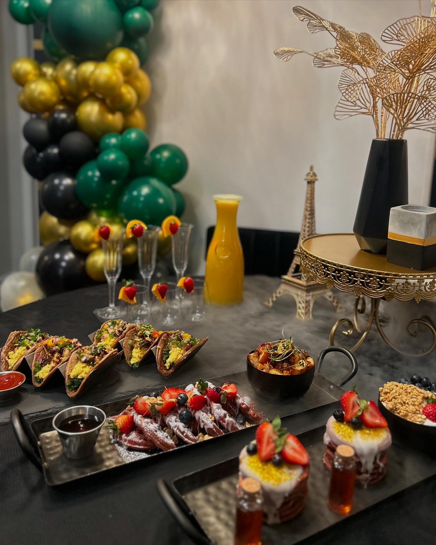 Table with desserts, drinks, and decorations including balloons, vases, and a decorative stand.