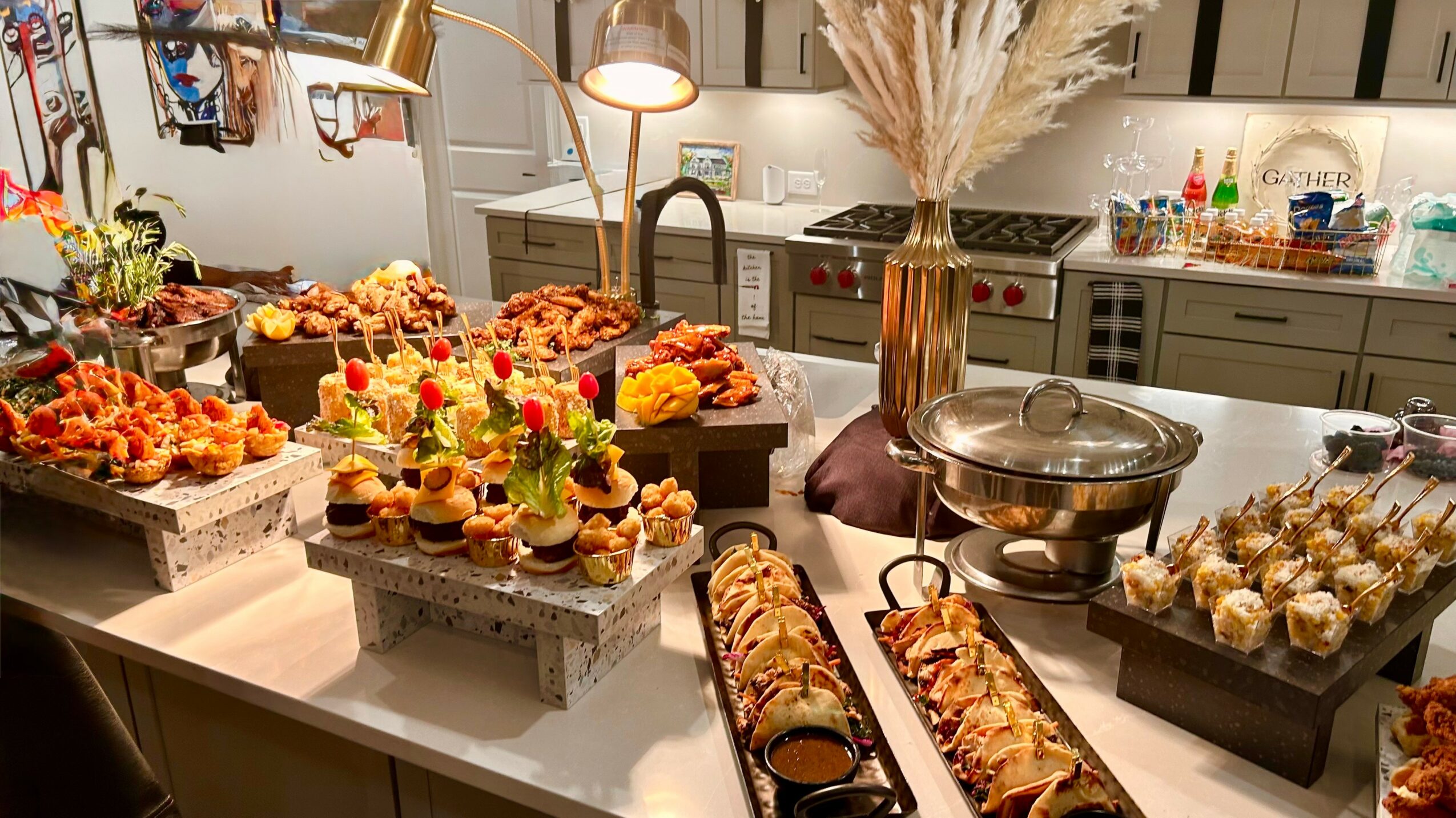 Kitchen counter with various decorated desserts and snacks, including cupcakes, pastries, and a large glass dish, with a vase of dried flowers.