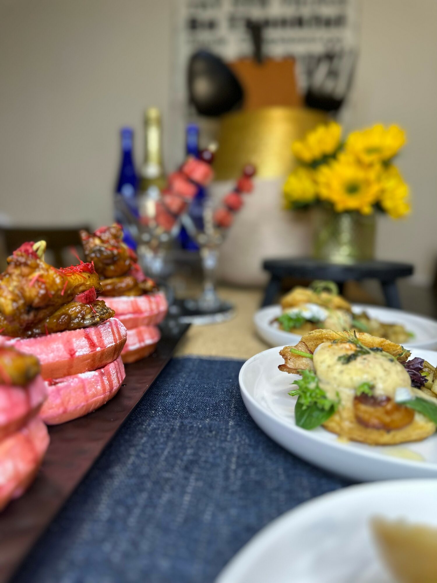 Plate with small sandwiches topped with cheese and greens, and a tray of cooked shrimp with pink shells, on a table.