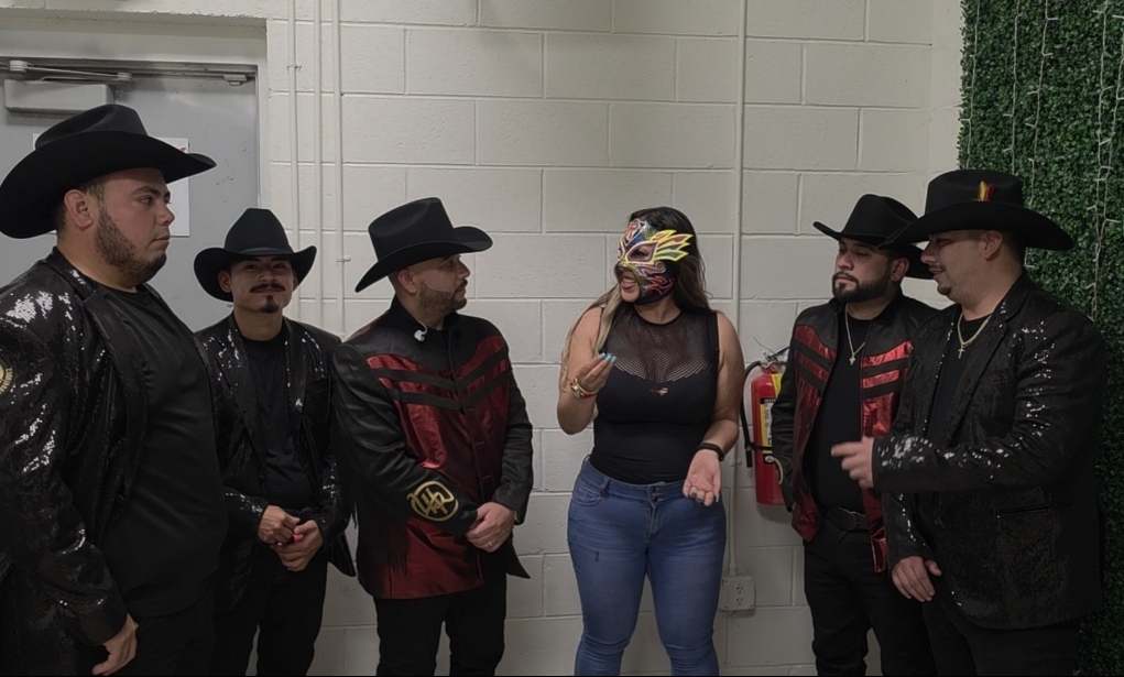 Group of six people, five men in black and red outfits with hats, one woman in a black top and jeans, holding a mask.