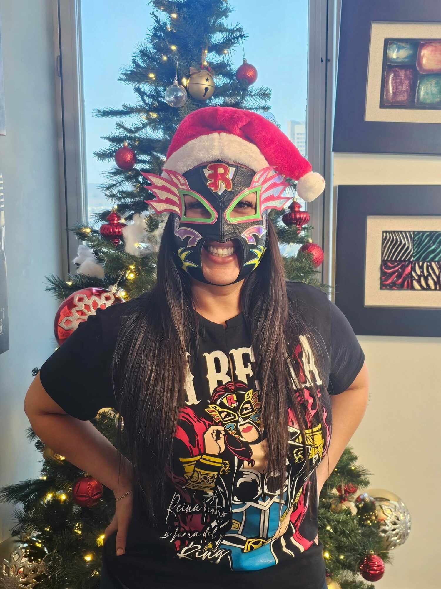 Person wearing a colorful clown mask and Santa hat, standing in front of decorated Christmas tree indoors.