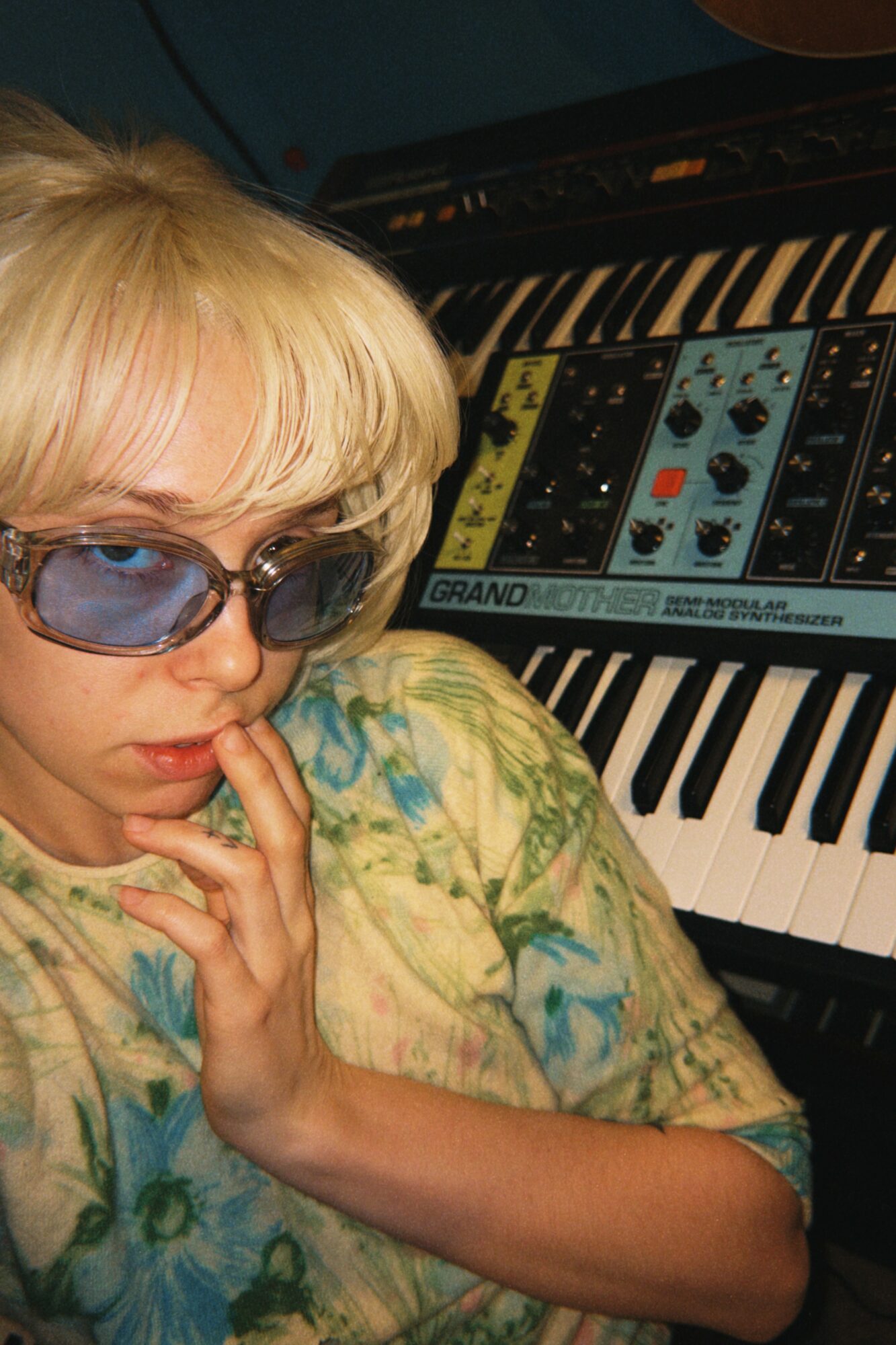 Person with blonde hair and sunglasses near a keyboard with a screen displaying music software.