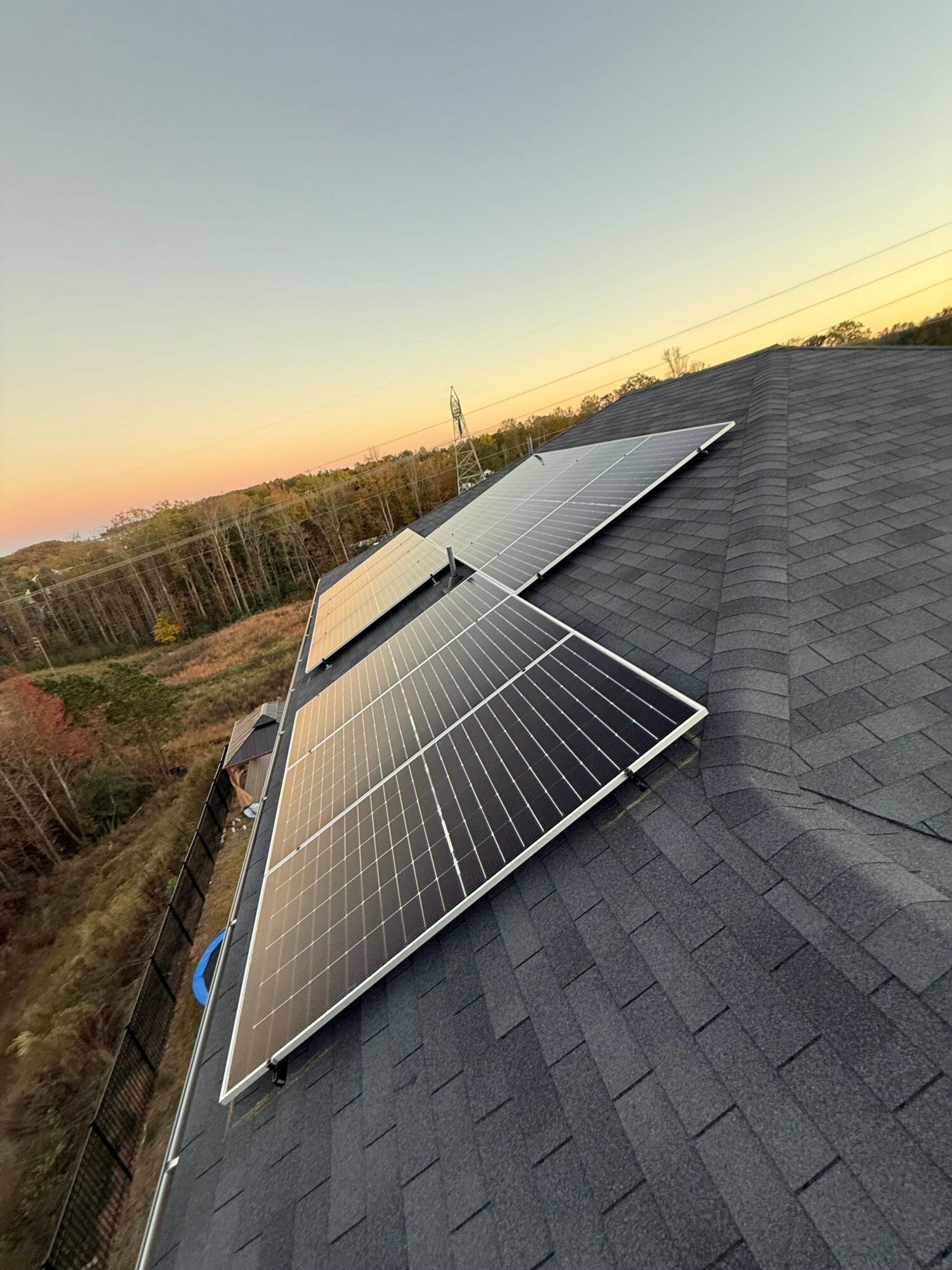 Multiple solar panels installed on a sloped roof during sunset, with a landscape and power lines in the background.