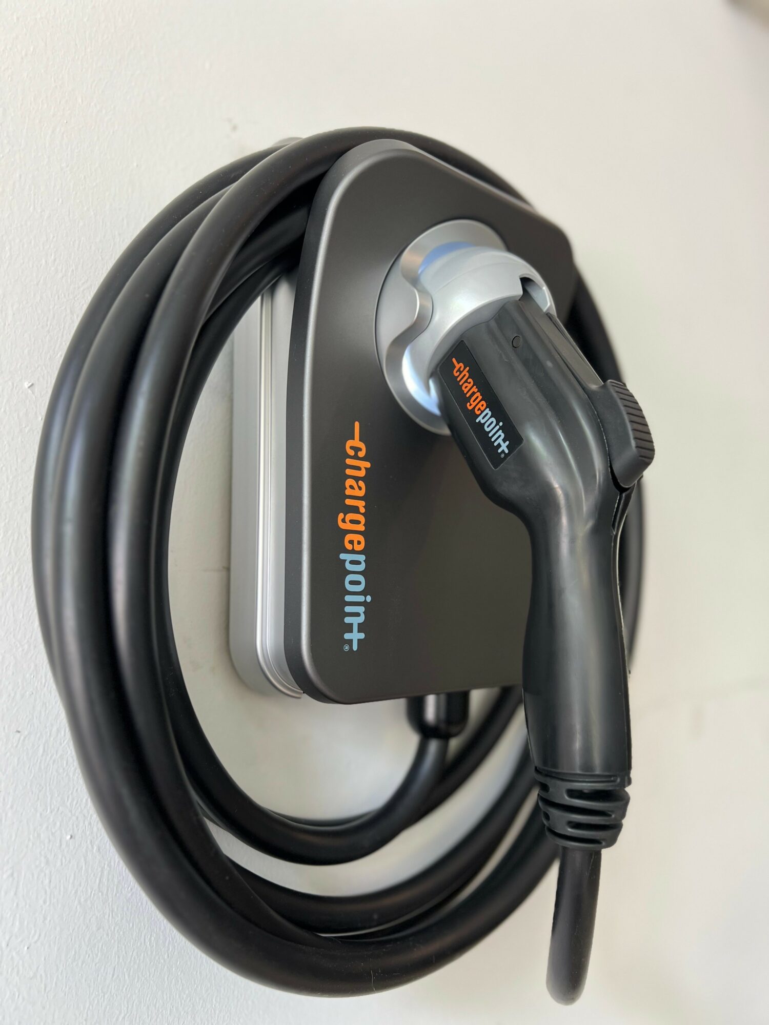Electric vehicle charging connector attached to a black charging station with a coiled cable.