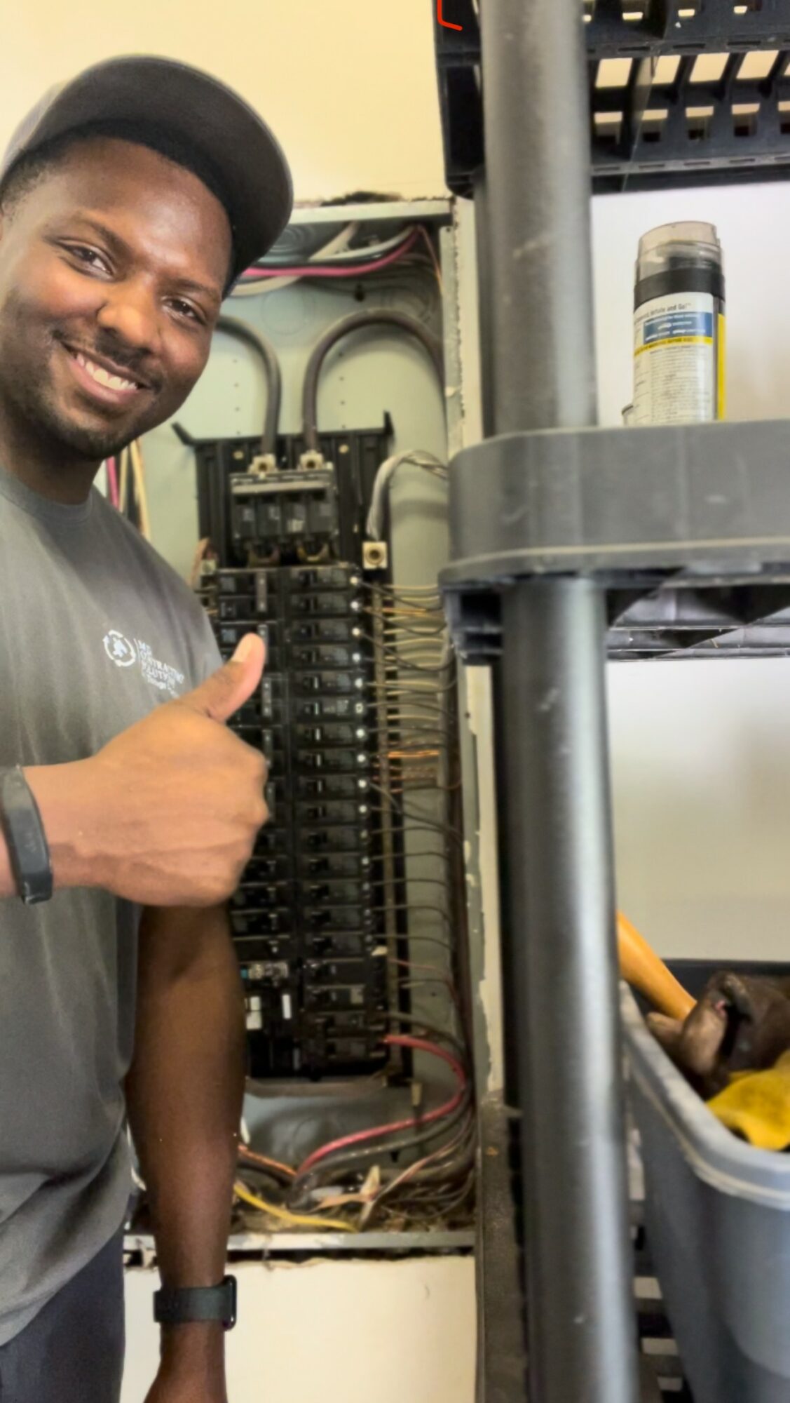 Person smiling and giving a thumbs-up next to electrical panel with wires and circuit breakers.