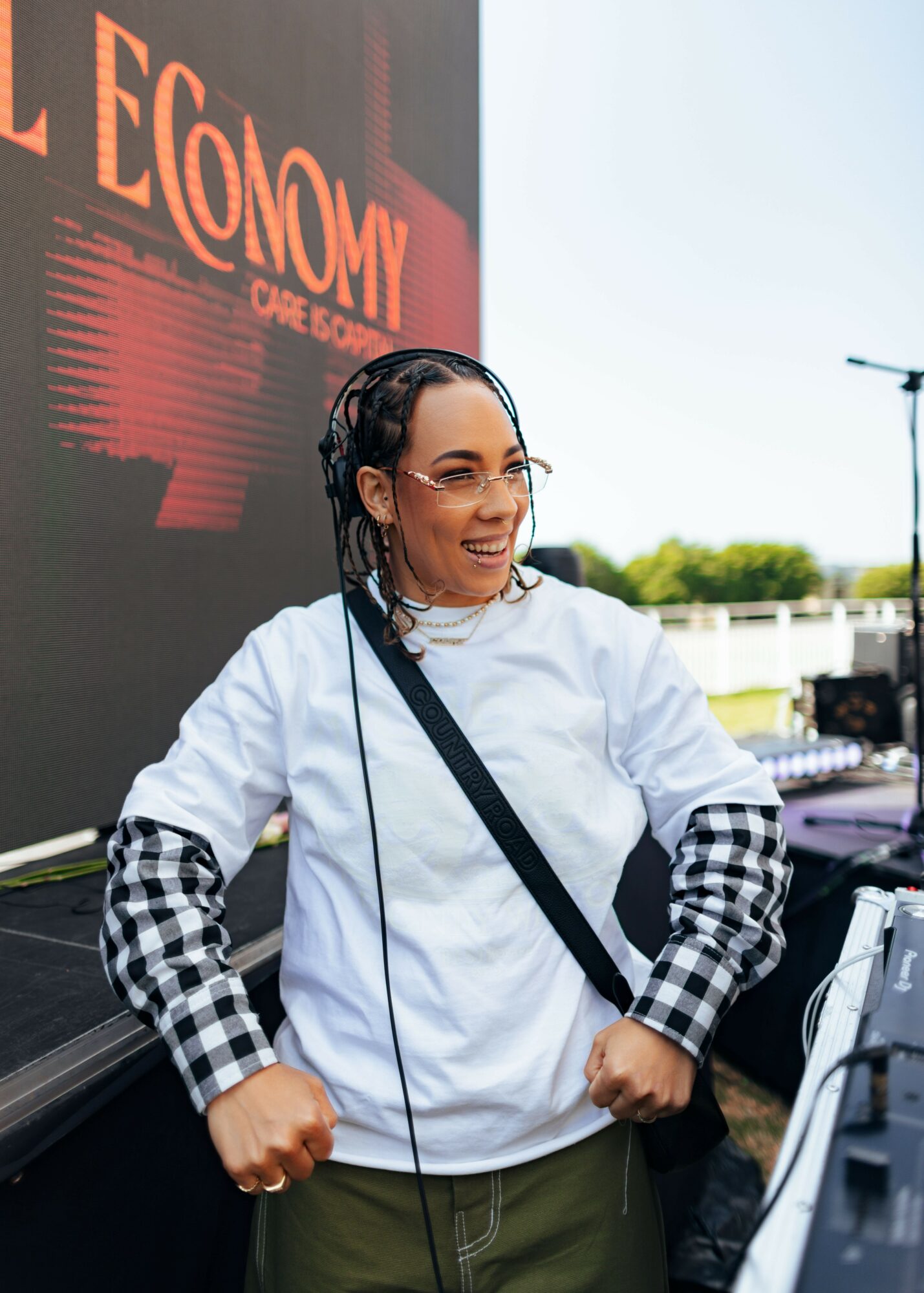 Woman with glasses and braided hair wearing a white jacket and checkered sleeves outdoors.