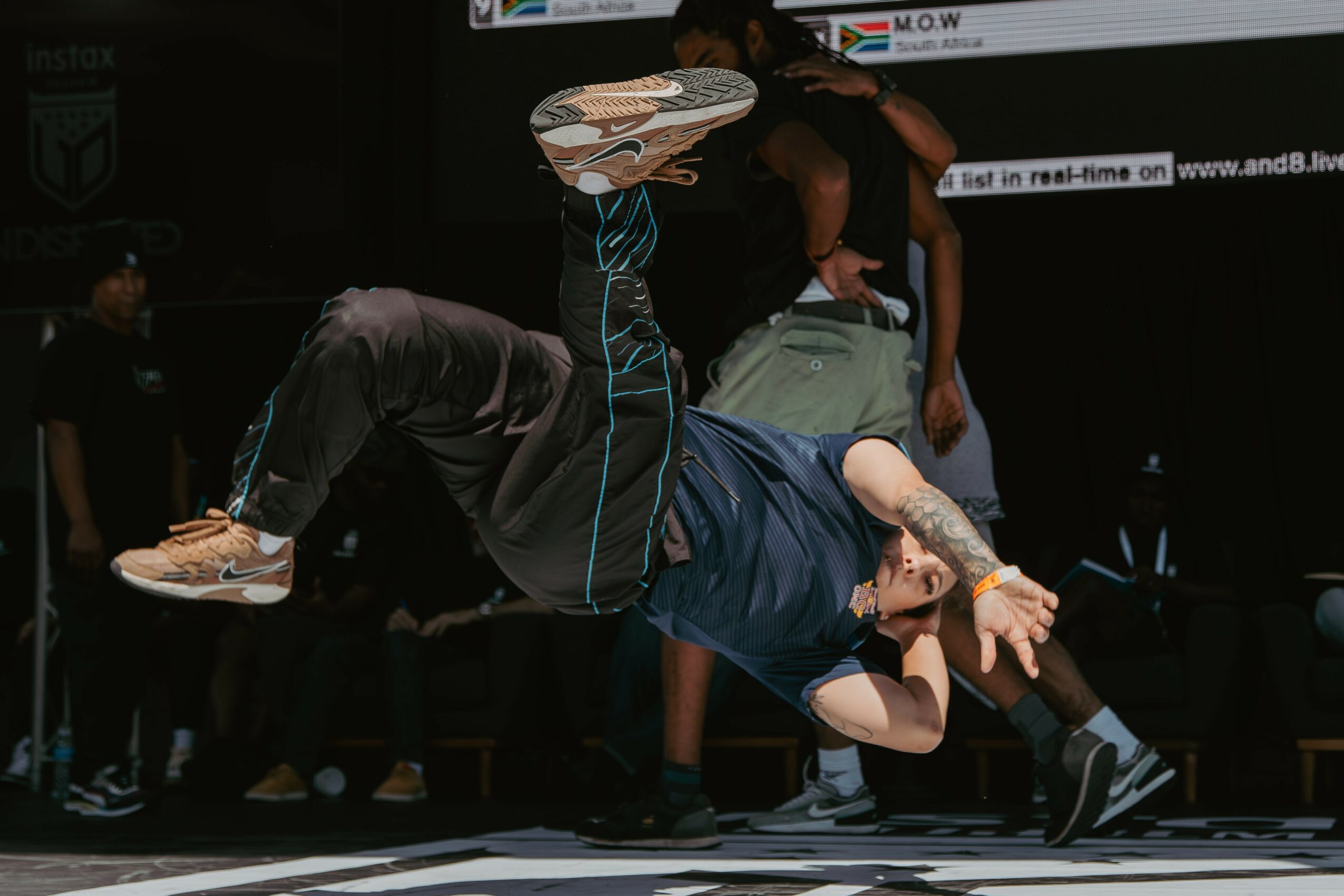 Person performing a breakdancing move on the floor with others watching in the background.