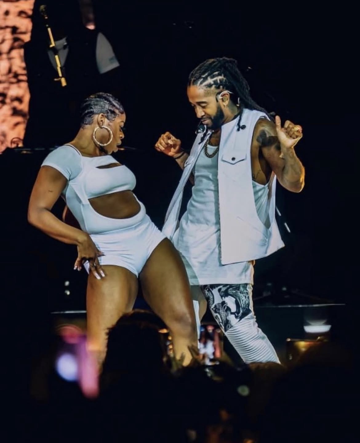 Two people dancing on stage, smiling, with dark background and audience in foreground.