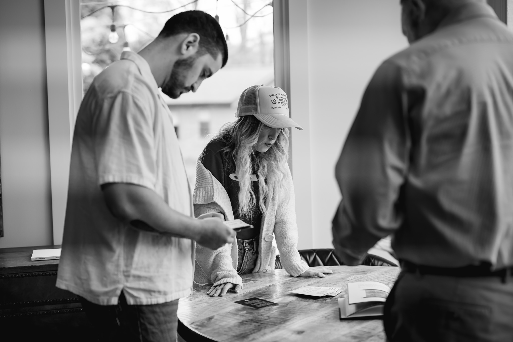Three people gathered around a table, looking at papers, in a room with large windows, black and white photo.