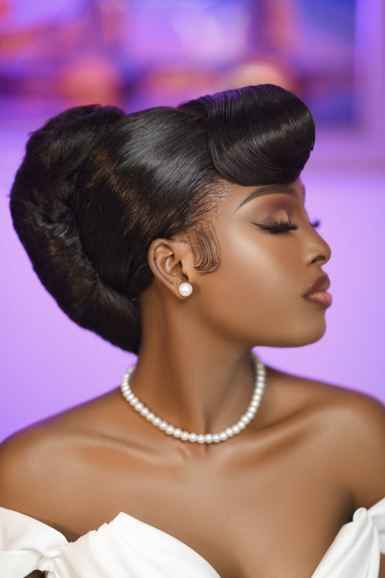 Elegant woman with styled hair, pearl necklace, and earrings, facing profile with closed eyes.