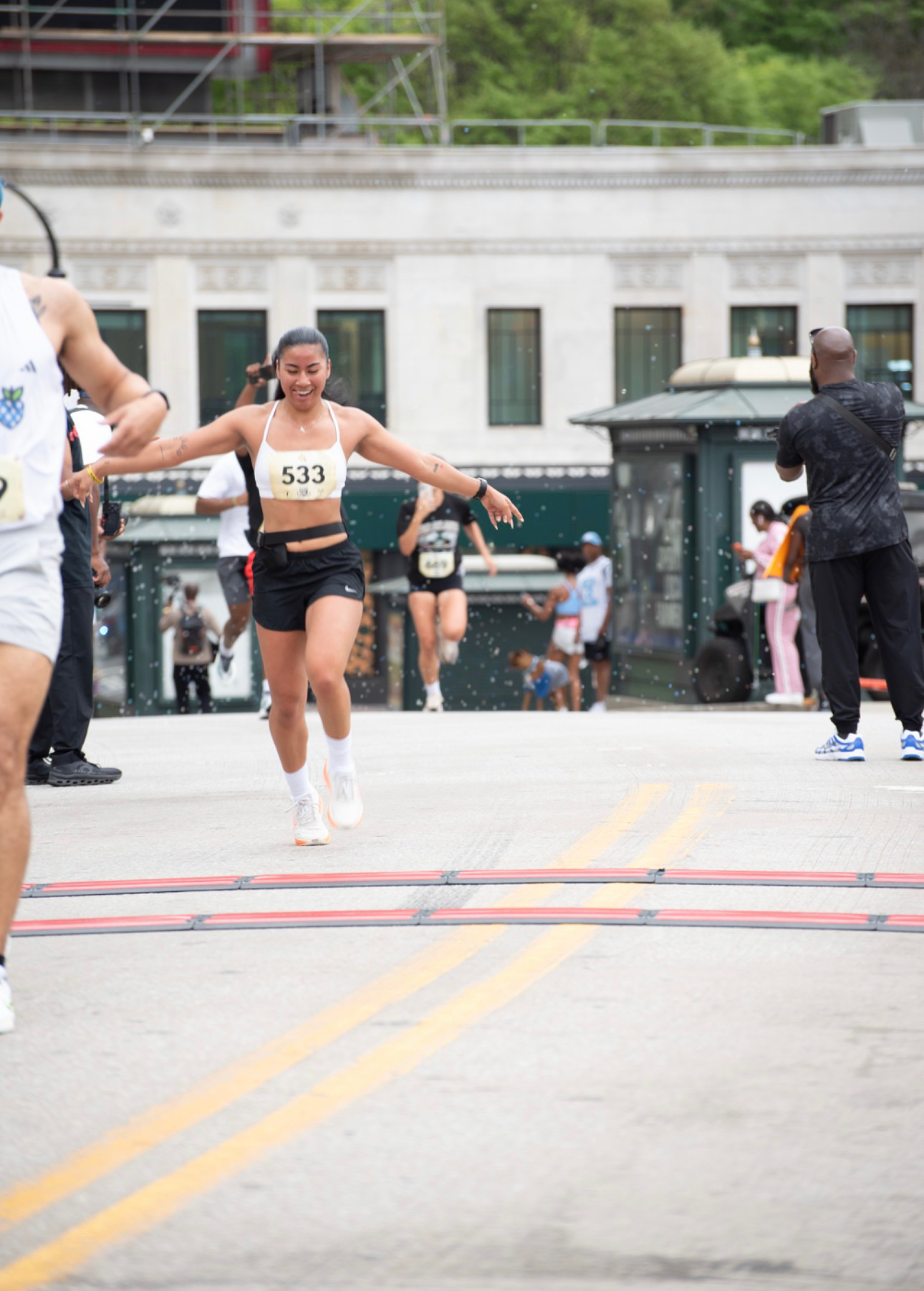 Female runner crossing finish line with arms outstretched, wearing a bib number 533, in an urban setting.