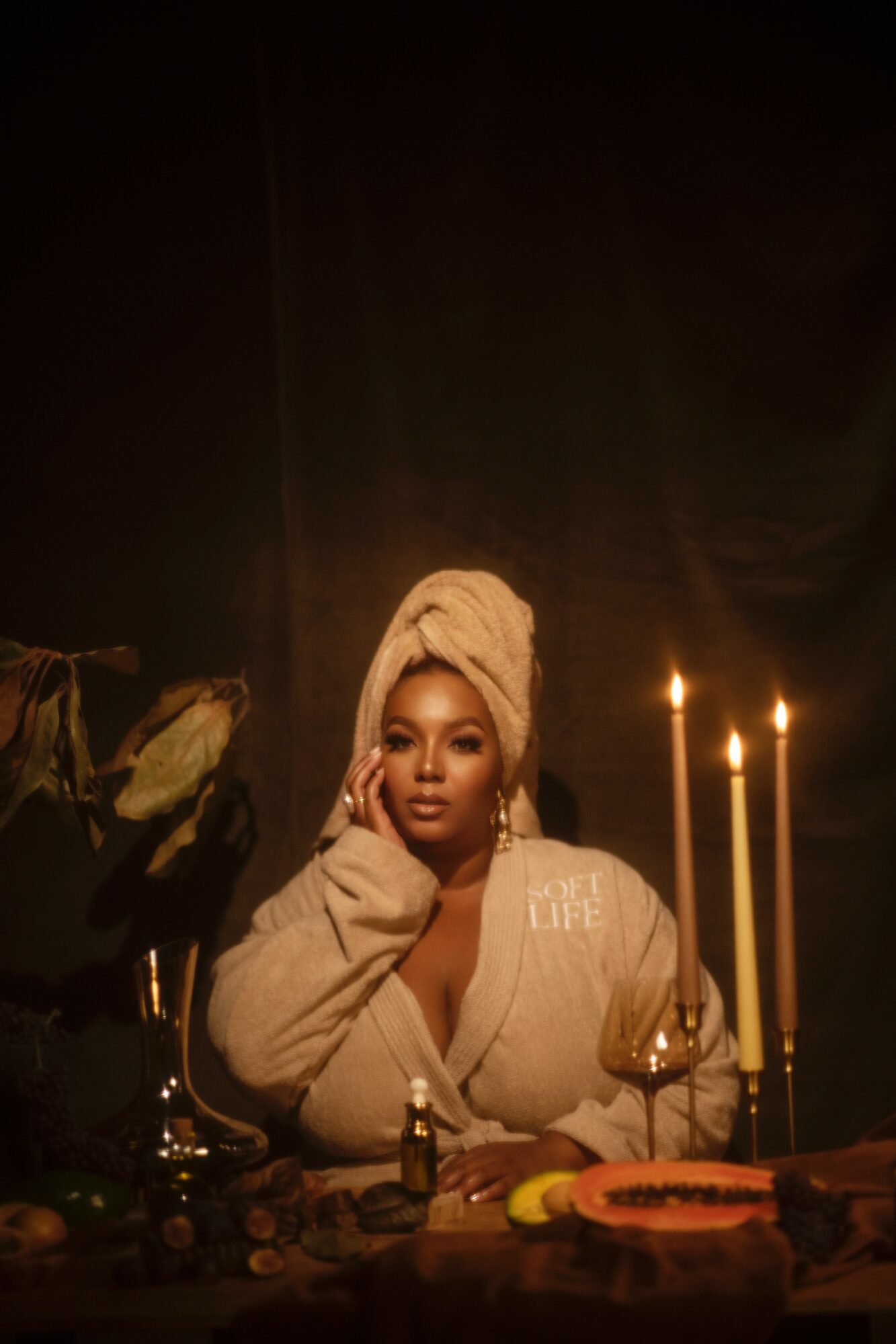 Woman with a towel wrapped around her head, sitting at a table with candles and decorative items, in a dark setting.