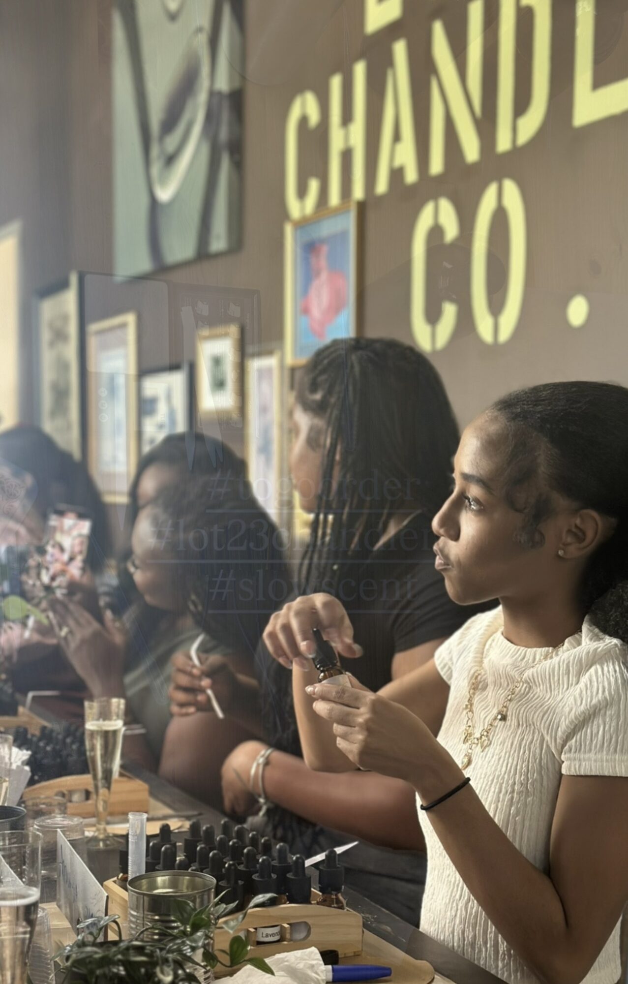 Group of people standing at a bar or counter, some holding drinks, with framed pictures and signs on the wall behind.