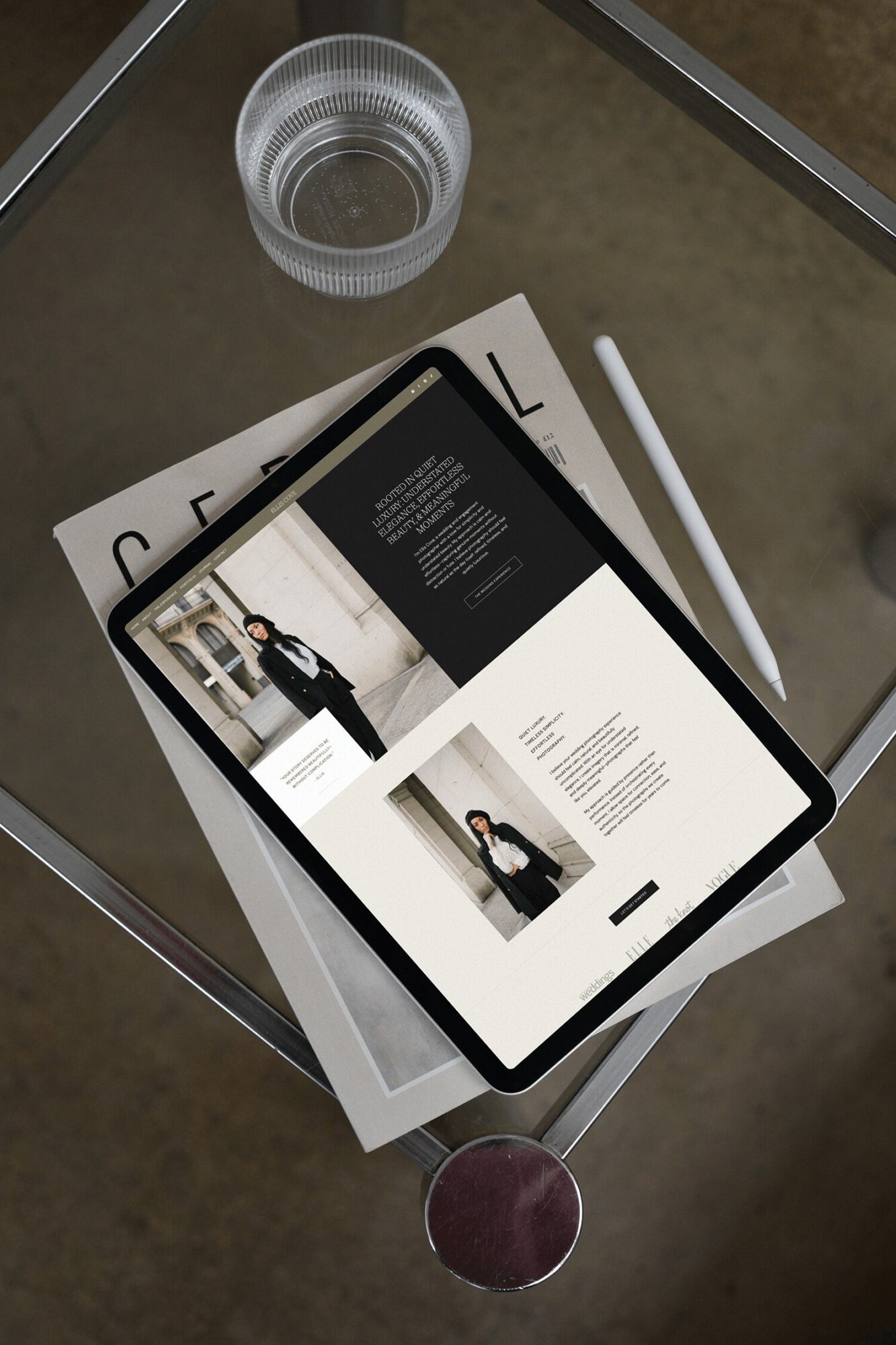 Tablet displaying a website with a person in a suit, placed on a glass table with a notebook, pen, and glass of water.