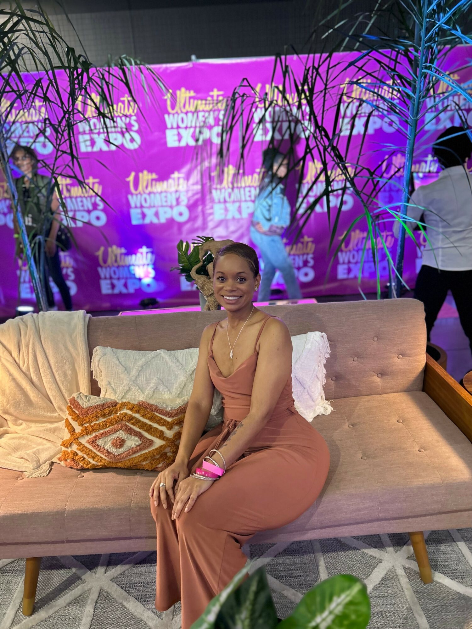 Woman sitting on a beige sofa with a purple background and trees, smiling at the camera.