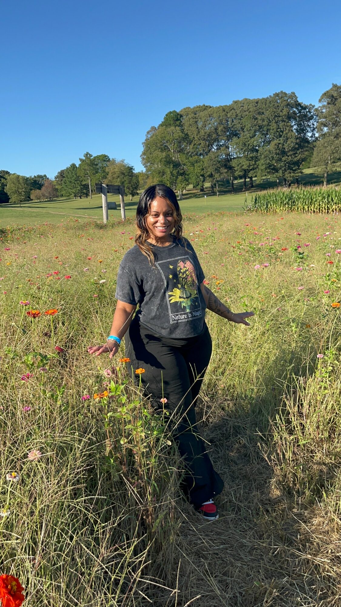 Woman walking through a grassy field with trees and blue sky in the background.