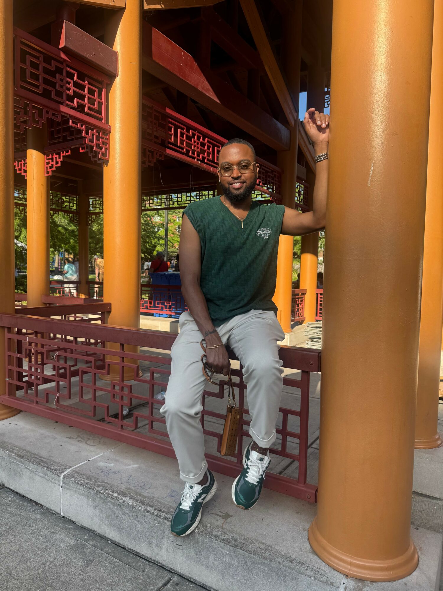 Man sitting on a bench, raising his right hand, in a traditional Asian architectural setting with orange columns and red decorative elements.