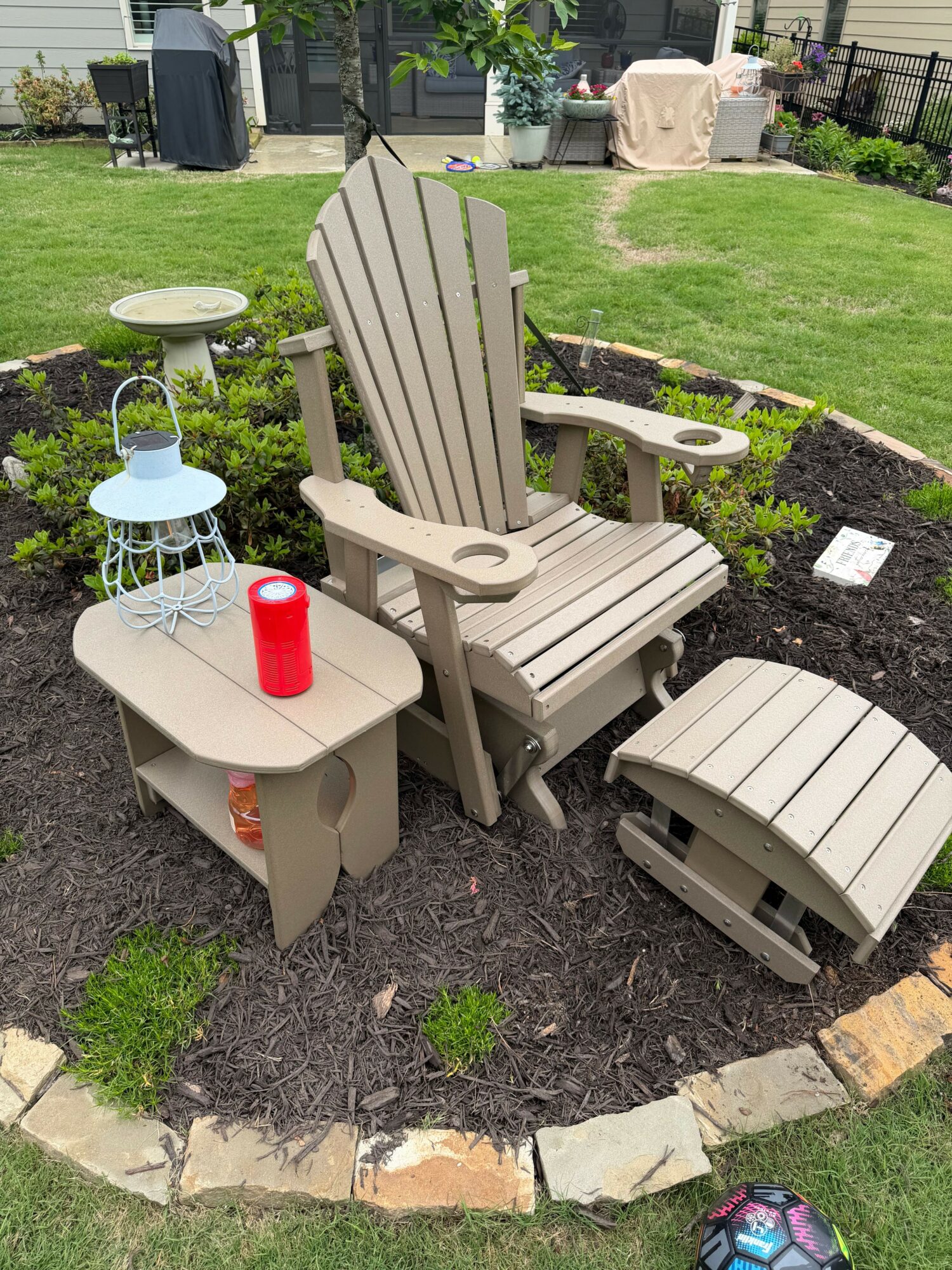 Adirondack chair with side table and footstool in a garden with grass and plants.