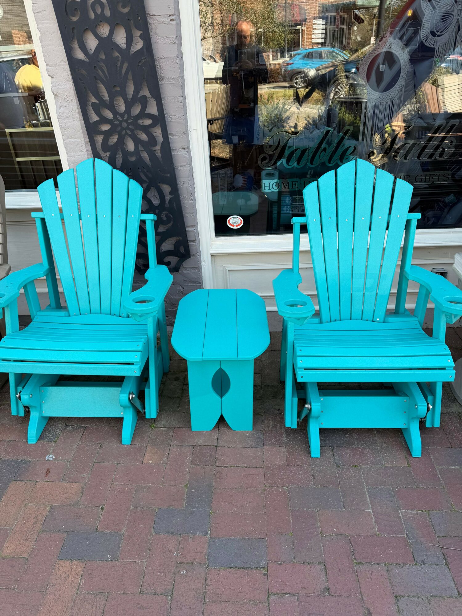 Two turquoise Adirondack chairs with a matching small table between them outside a building.