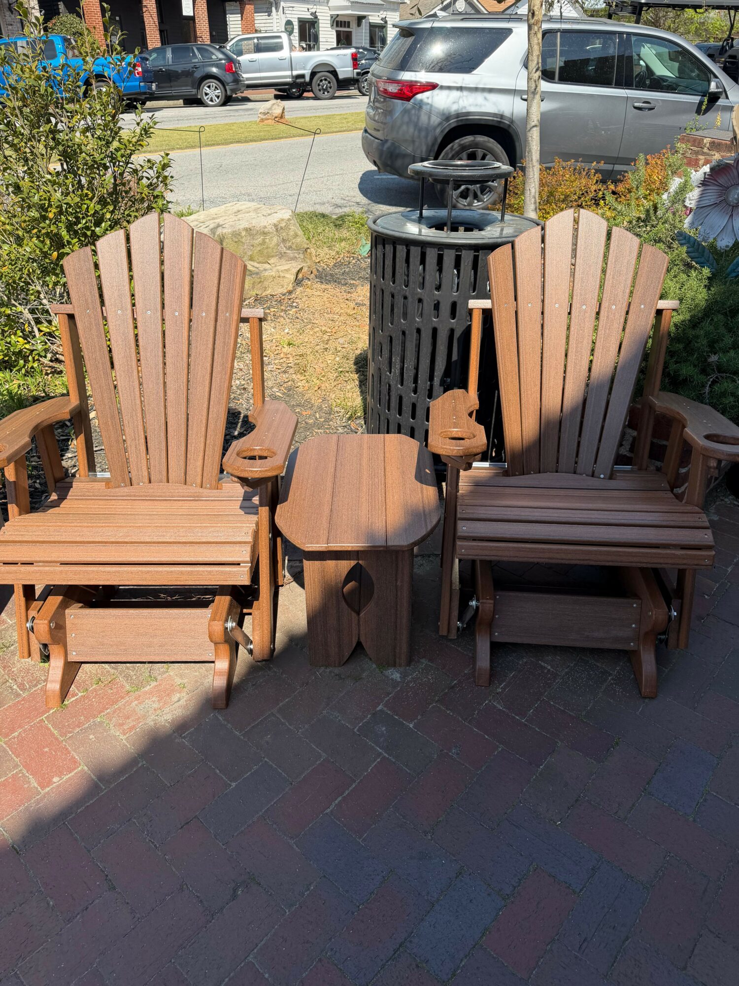 Two wooden outdoor chairs with armrests and a small table between them, on a brick patio.