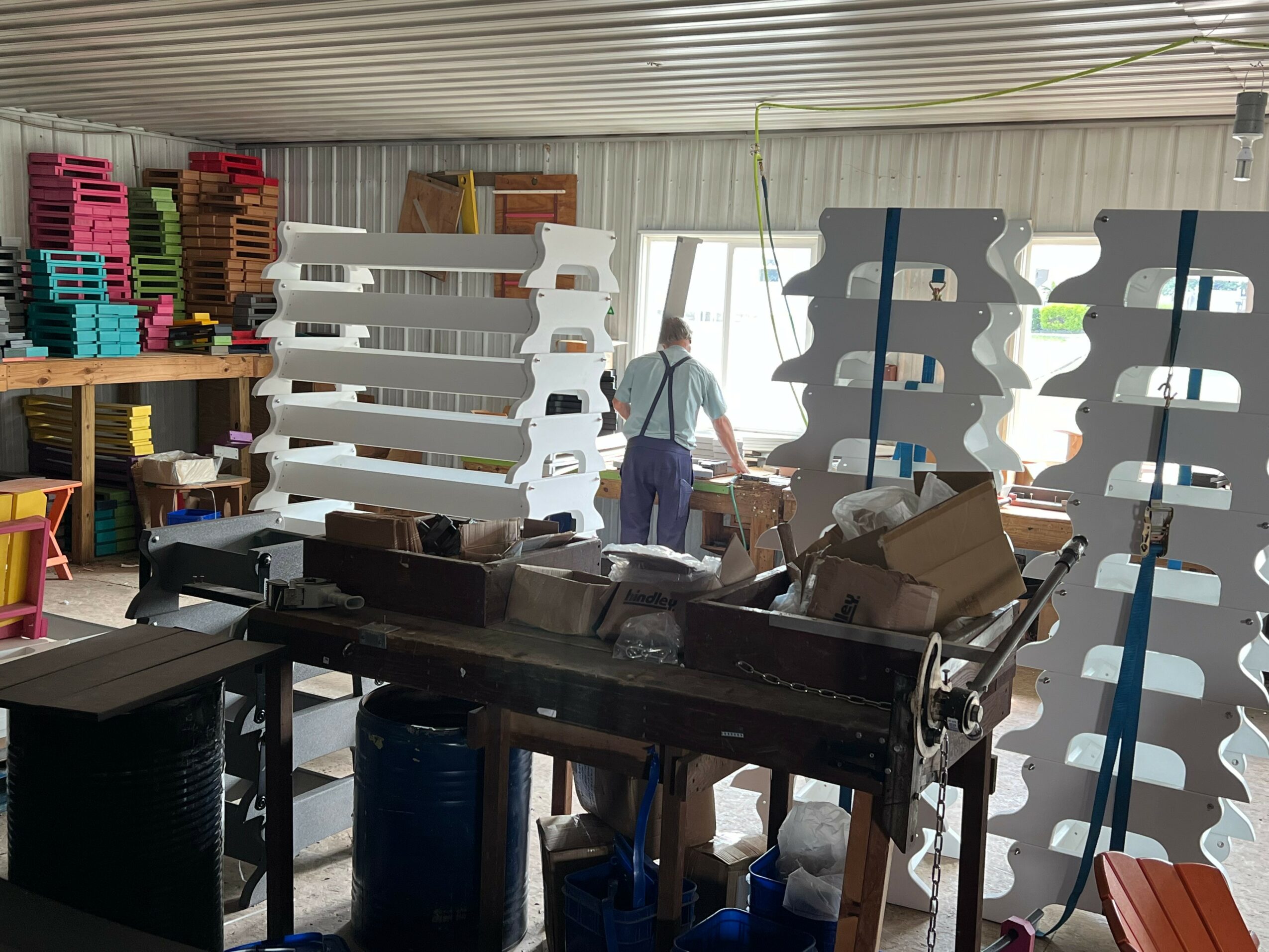 Person working in storage room with stacked plastic pallets and boxes, shelves, and a work table.